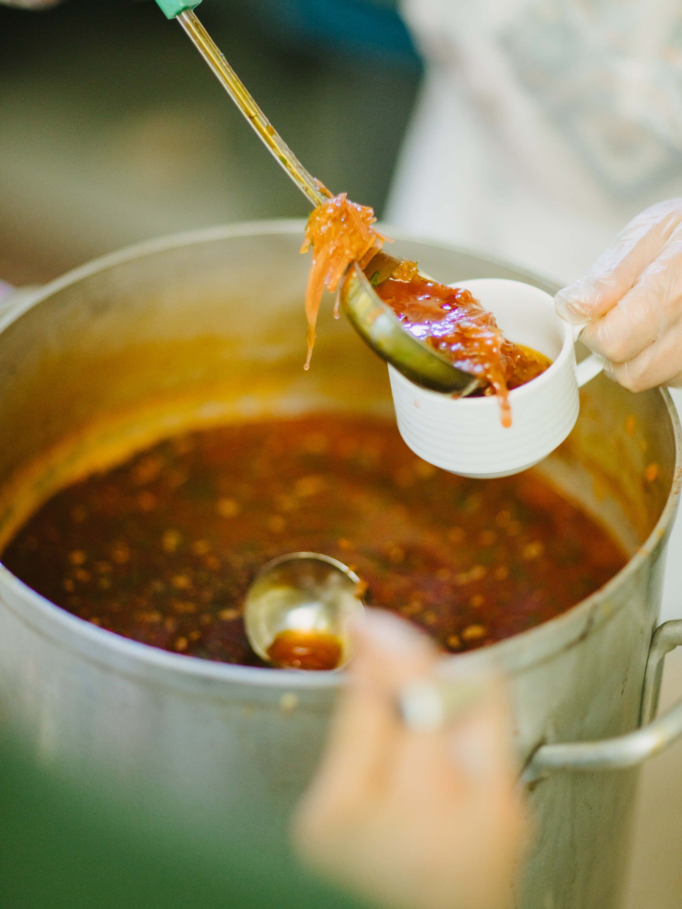A server ladles golden borscht into a white bowl at a Ukrainian fundraiser dinner, steam rising from the pot below