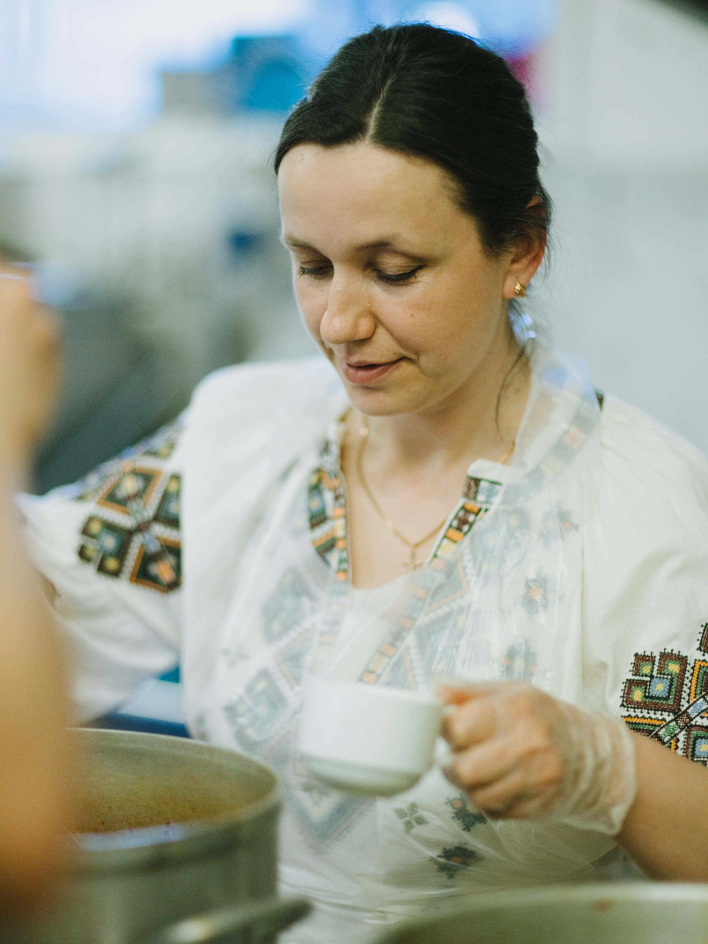 Woman in embroidered white linen smiles while ladling soup at a Ukrainian fundraiser dinner
