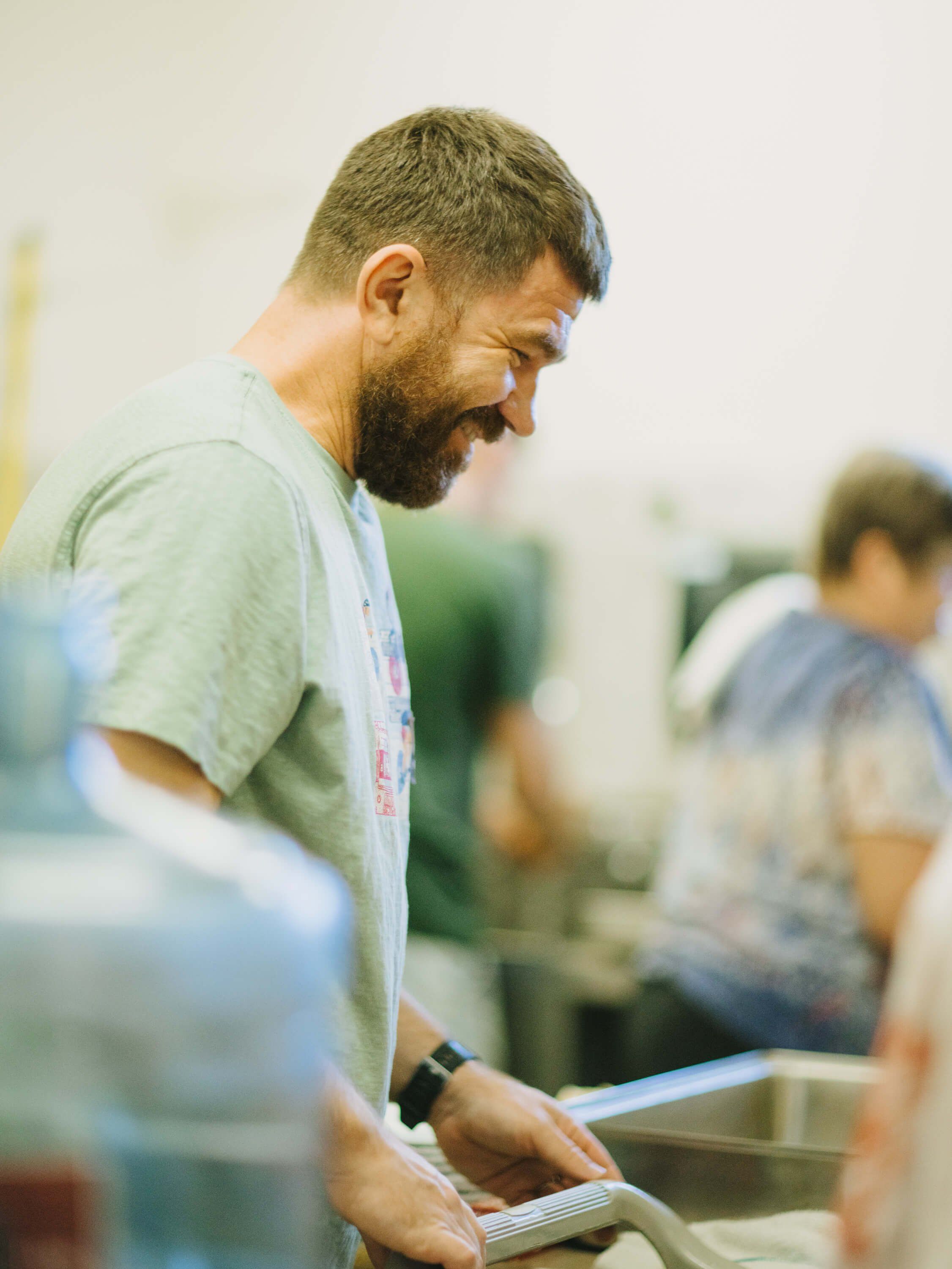 Man in sage green shirt smiles while serving food at an indoor community dinner event