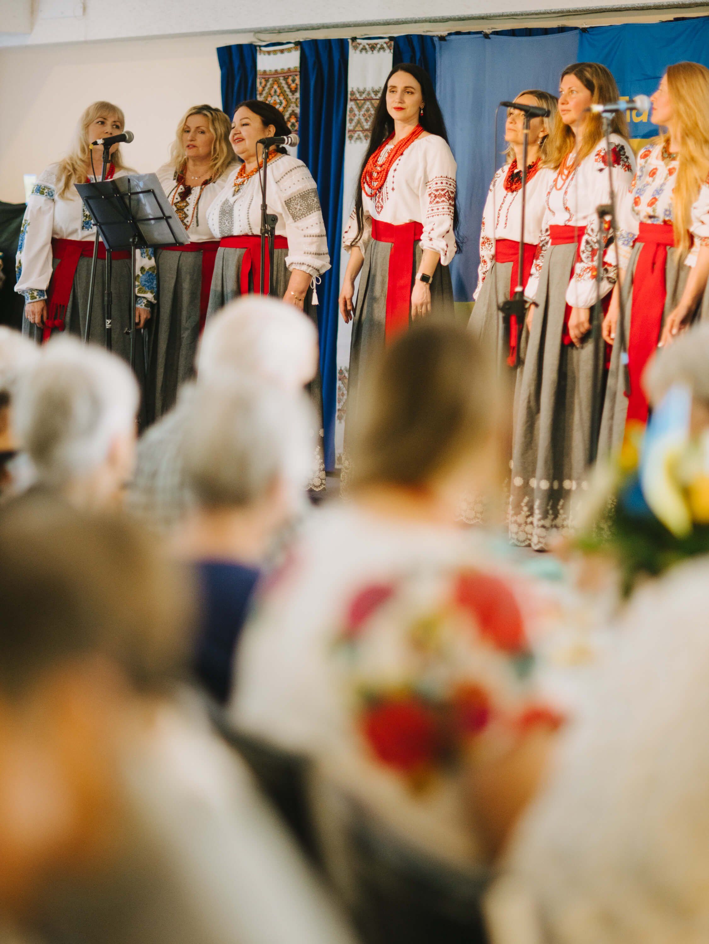 Ukrainian performers in traditional embroidered clothing perform for seated audience members at an indoor fundraiser dinner