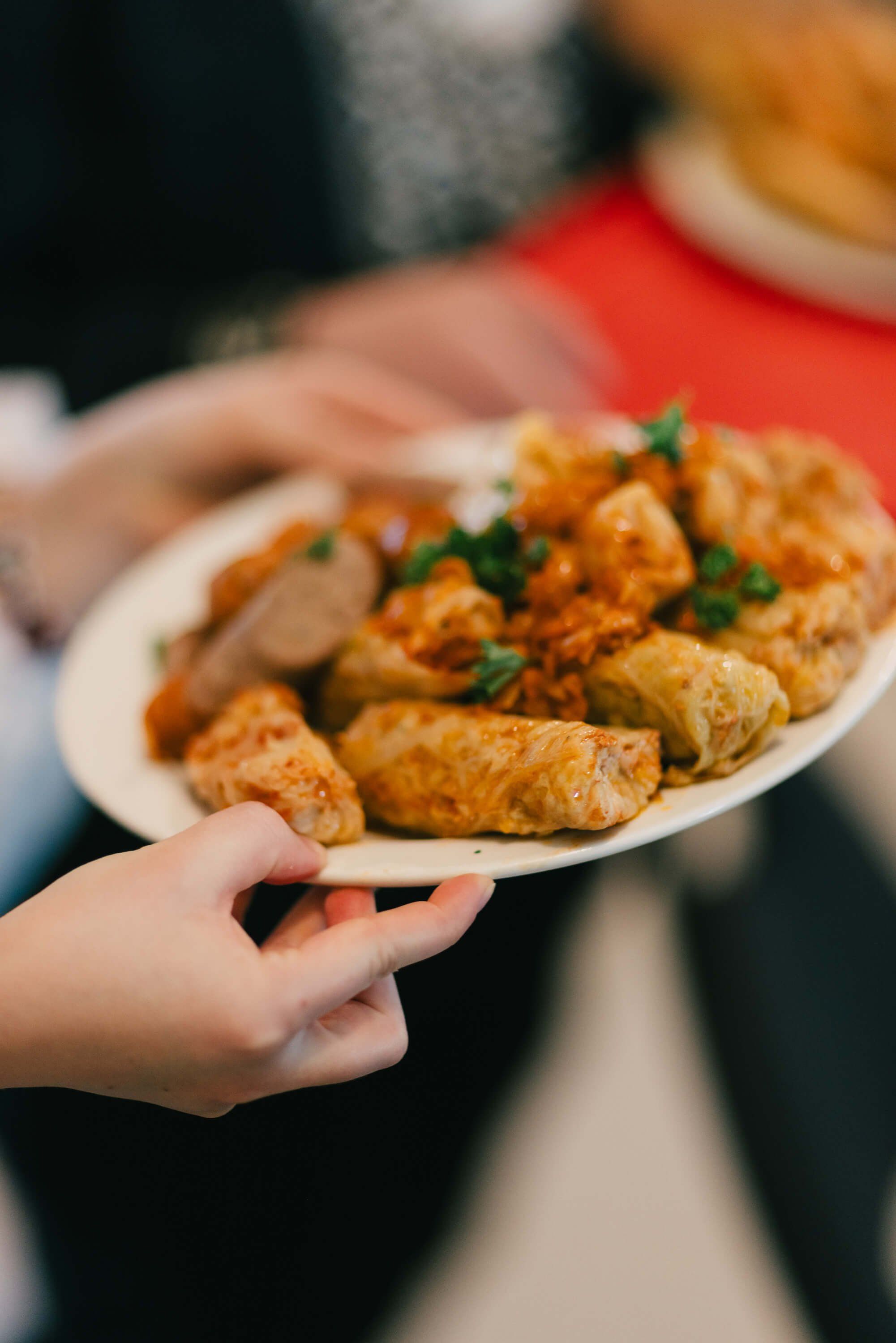 Hand holding a white plate of golden-fried Ukrainian pastries garnished with fresh parsley at an evening fundraiser dinner