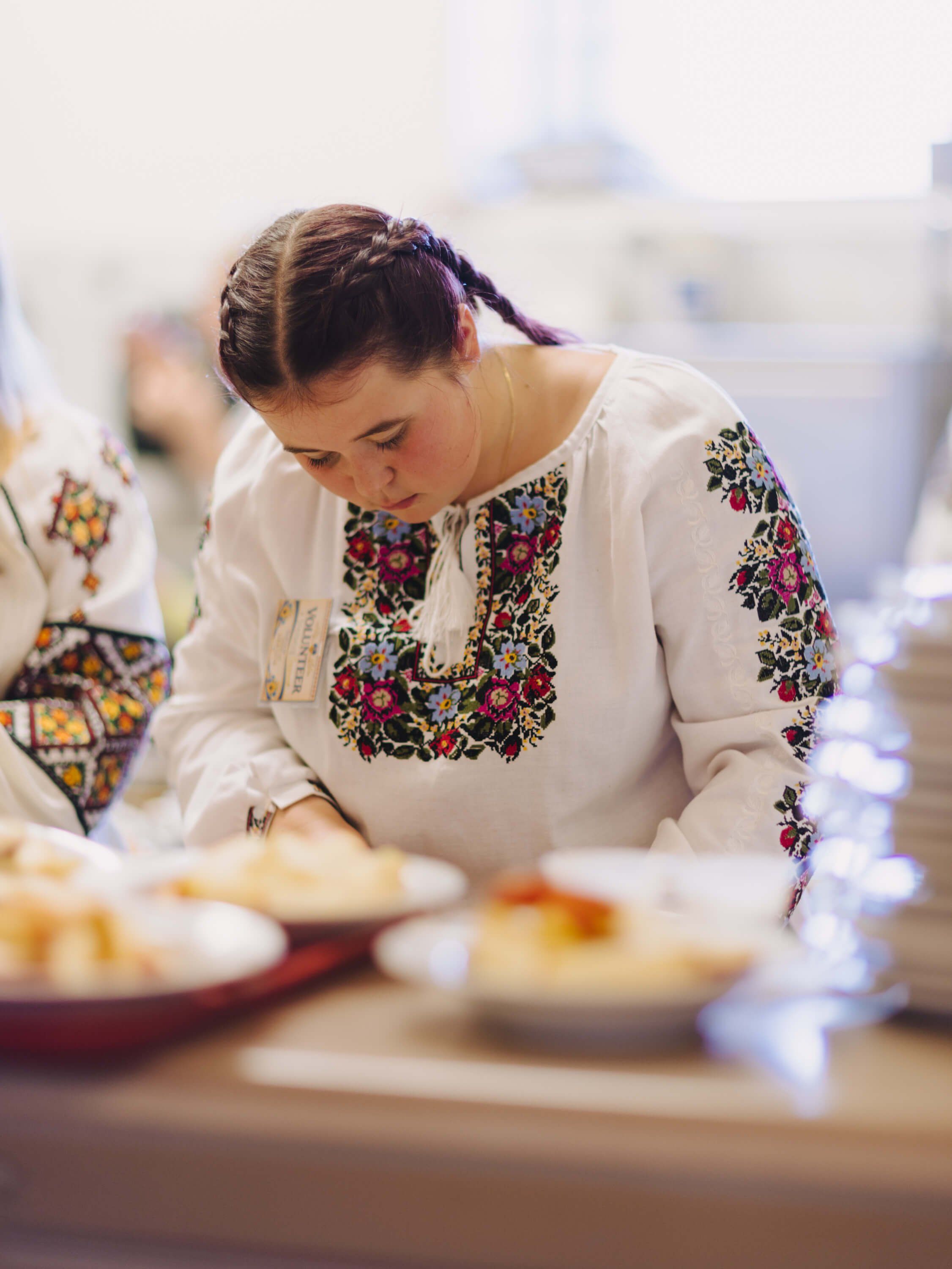 Woman in embroidered white linen blouse leans over a table of traditional dishes at a Ukrainian fundraiser dinner
