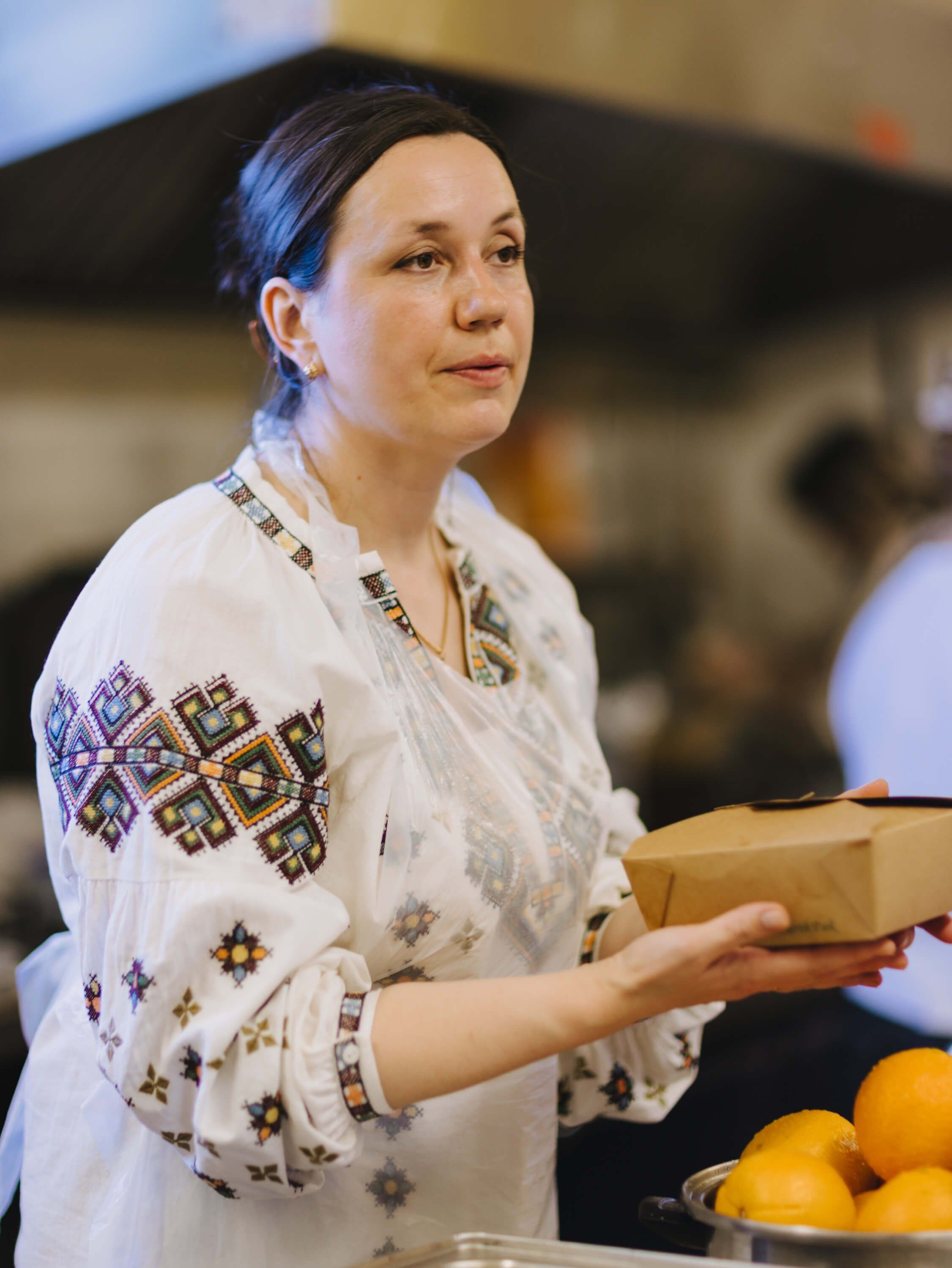 Woman in white embroidered blouse holding a gift box at the Ukrainian fundraiser dinner, warm indoor lighting