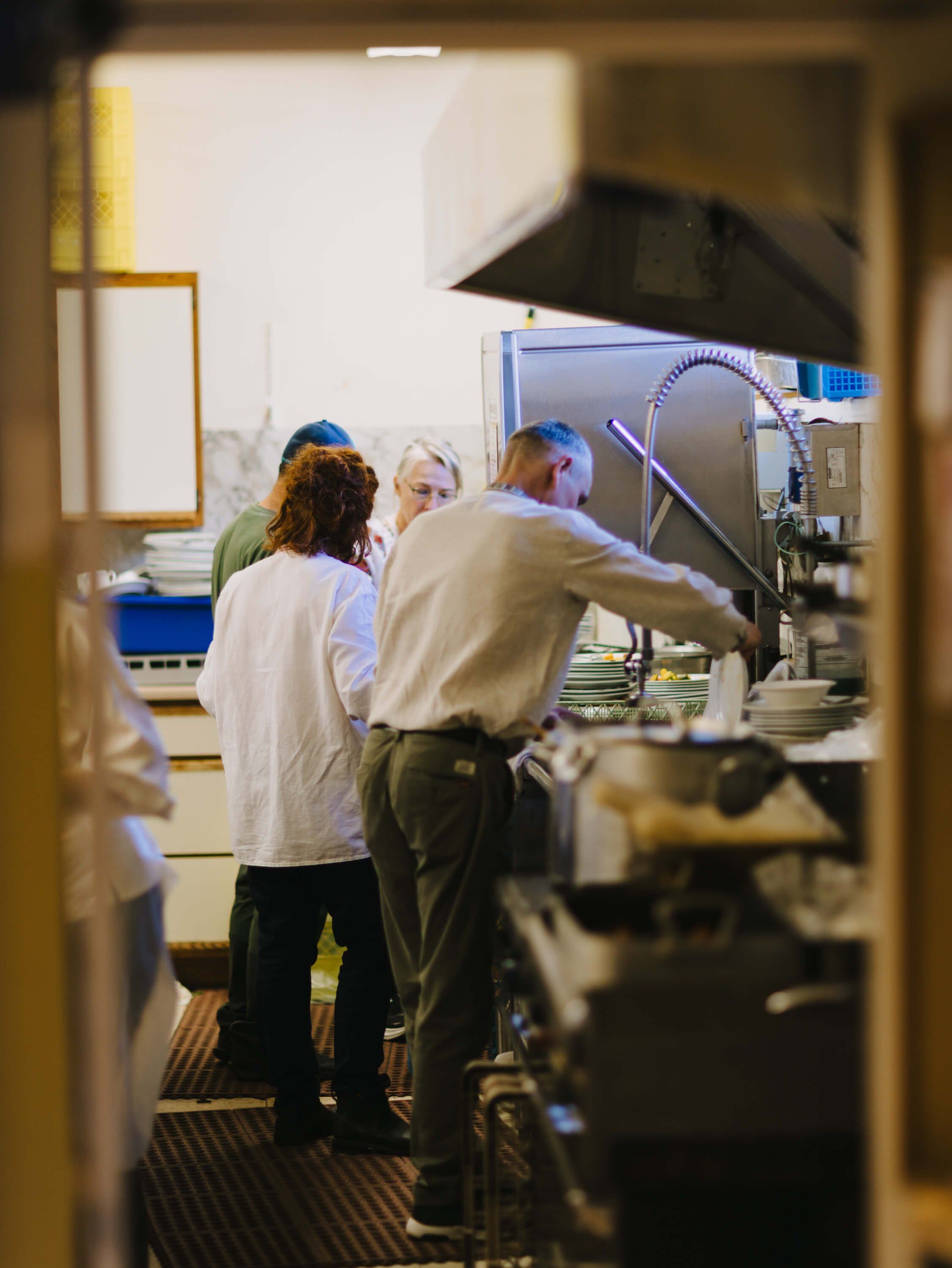 Kitchen volunteers in white coats work together at a stainless steel counter during the fundraiser dinner preparation