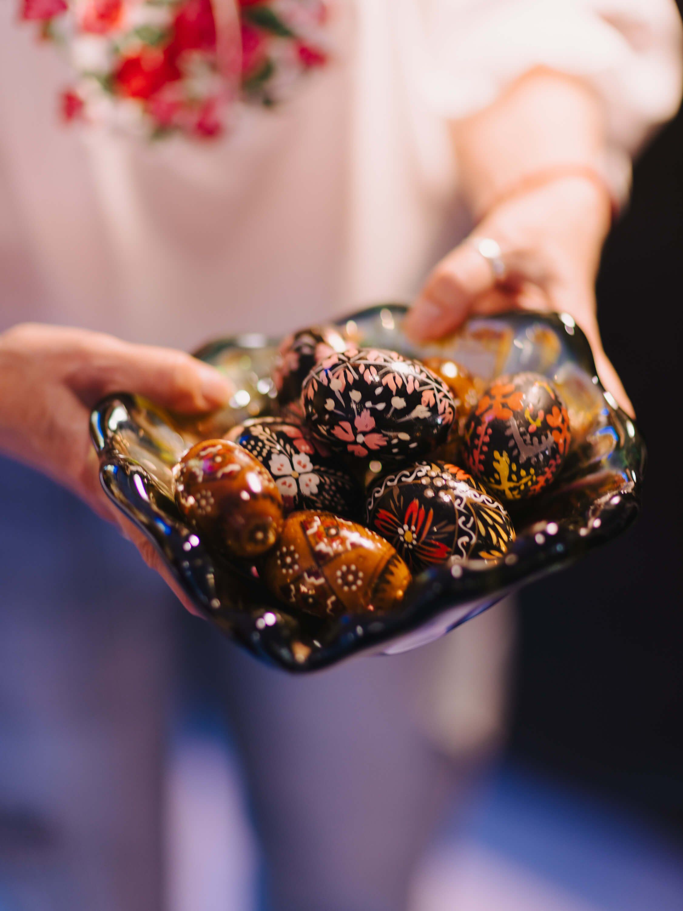 Hands holding a dark plate of gleaming chocolate-covered pastries at an evening fundraiser dinner