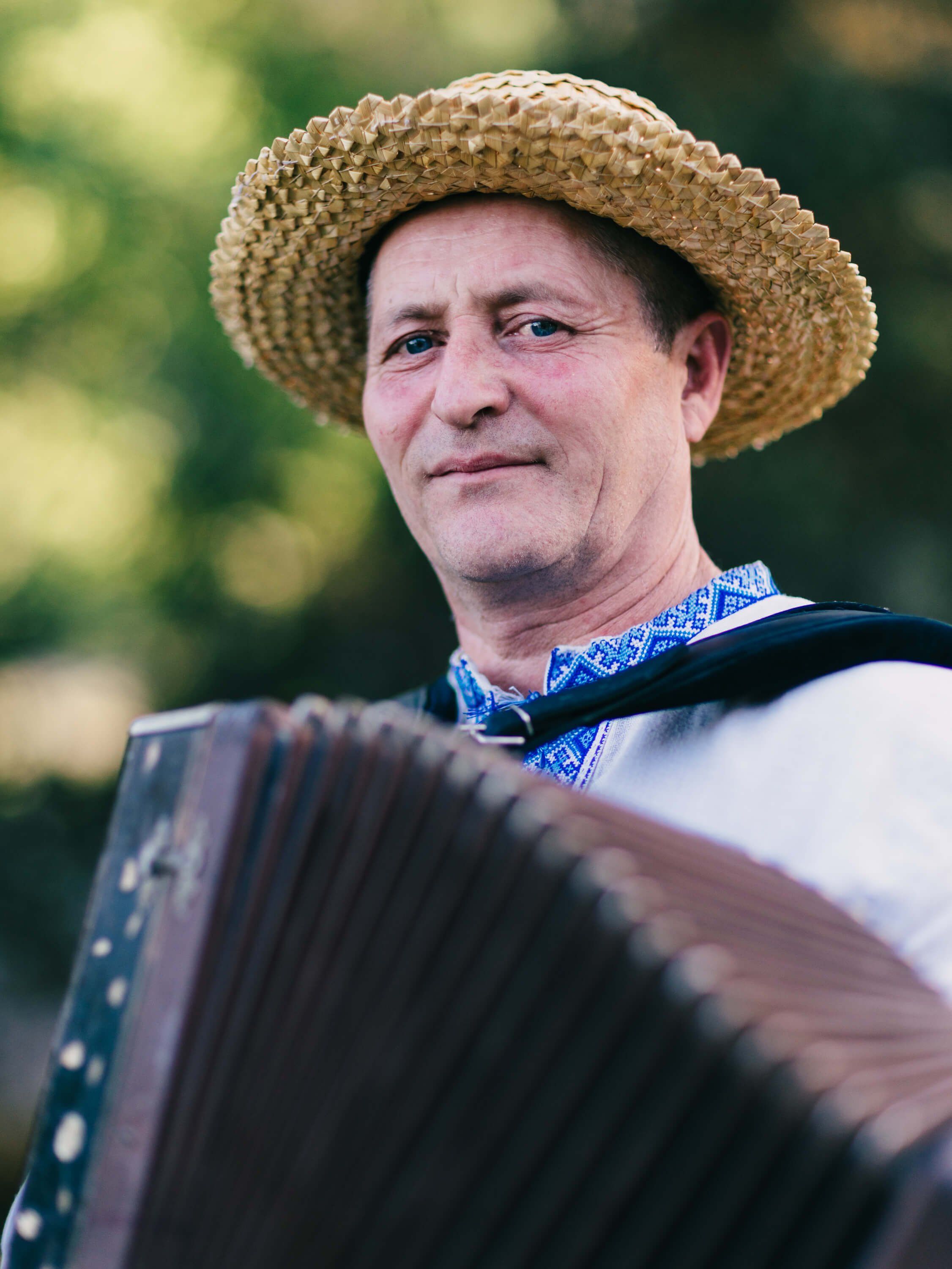 Man in straw hat and blue embroidered shirt plays accordion outdoors in golden afternoon light