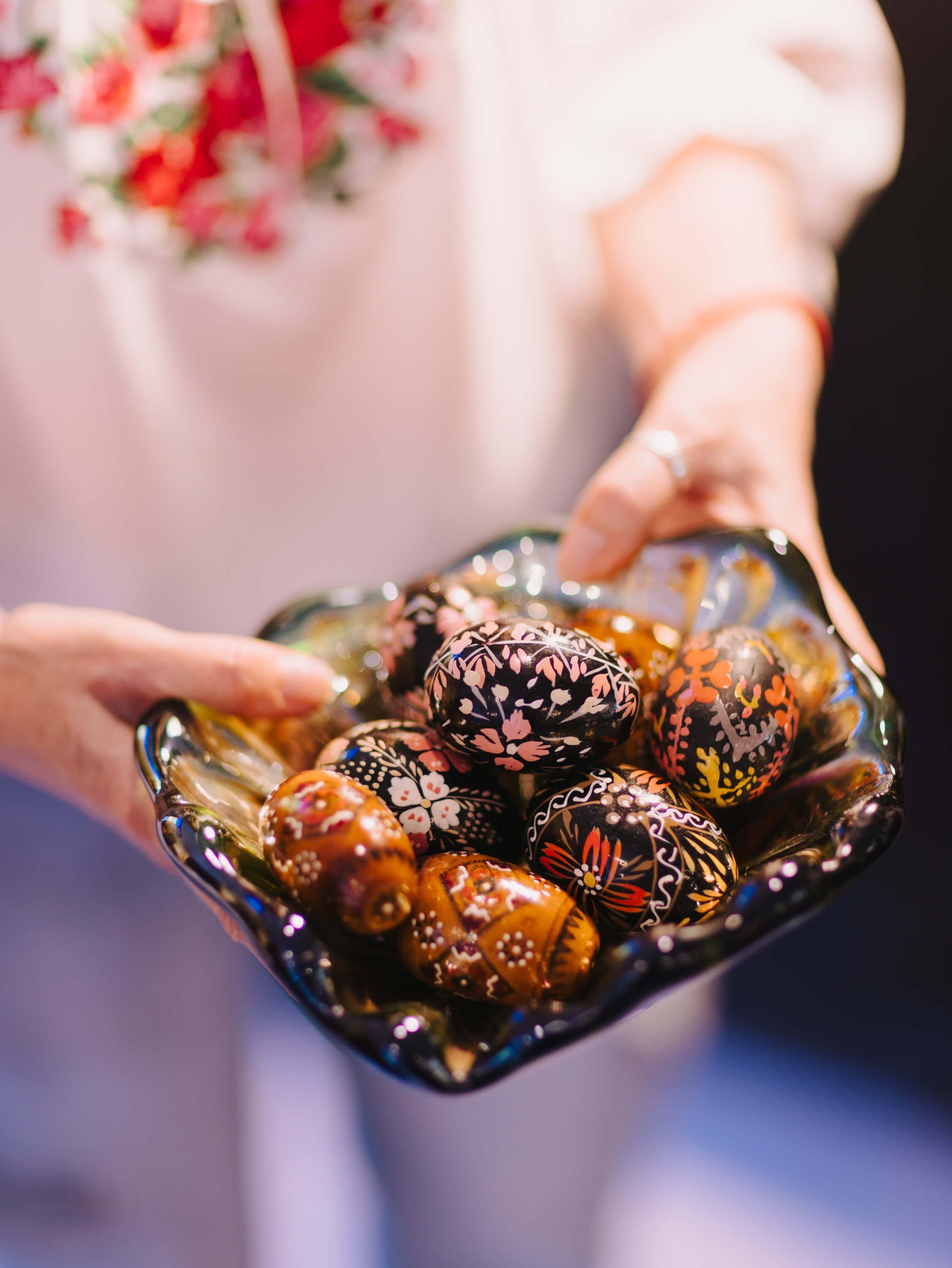 Hands in soft pink fabric hold a dark decorative bowl filled with ornate chocolate truffles at a candlelit evening event