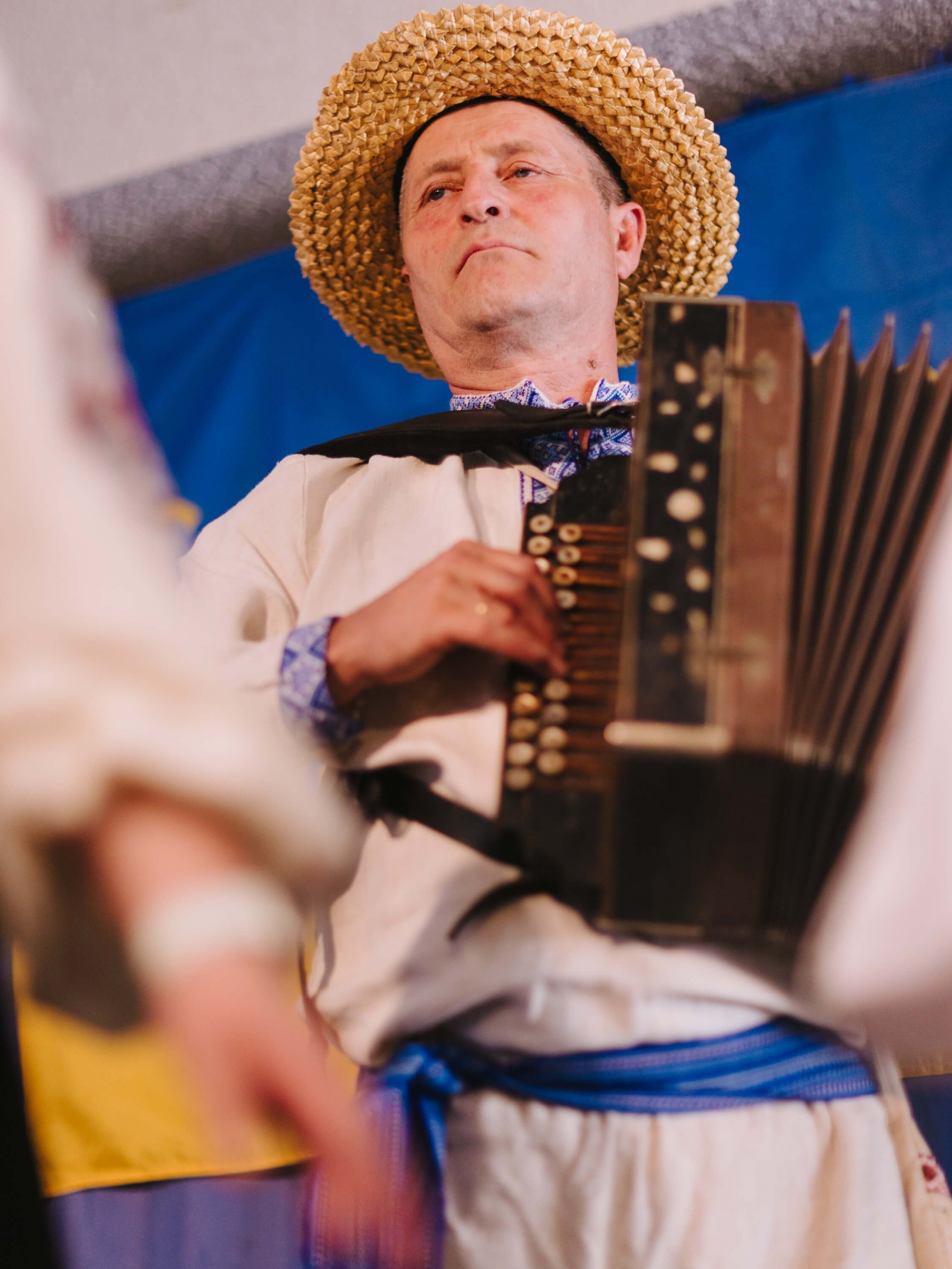 Man in straw hat and cream shirt plays button accordion at Ukrainian fundraiser dinner event