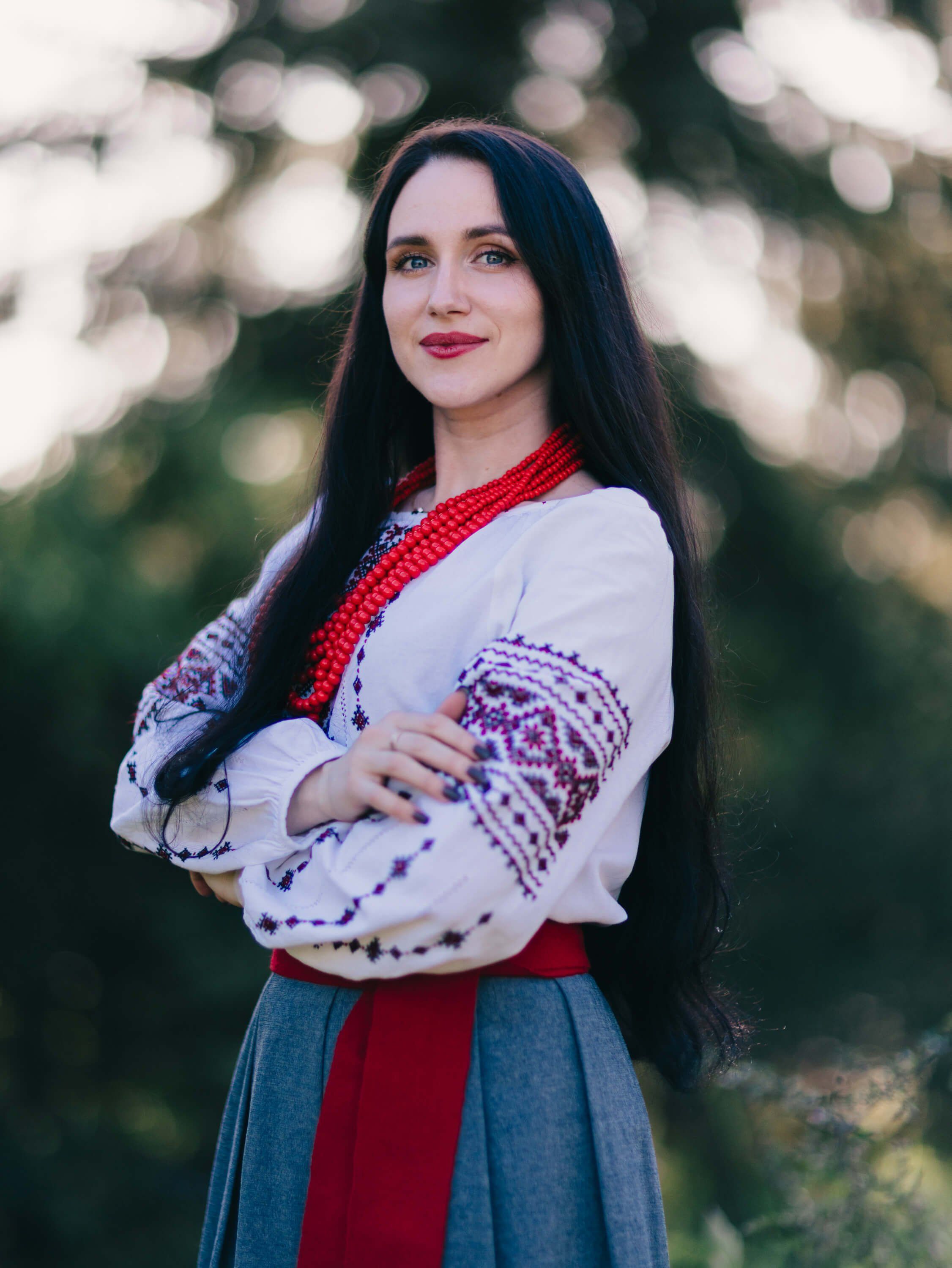 Woman in embroidered white blouse and red-and-blue skirt with red scarf poses outdoors at golden hour