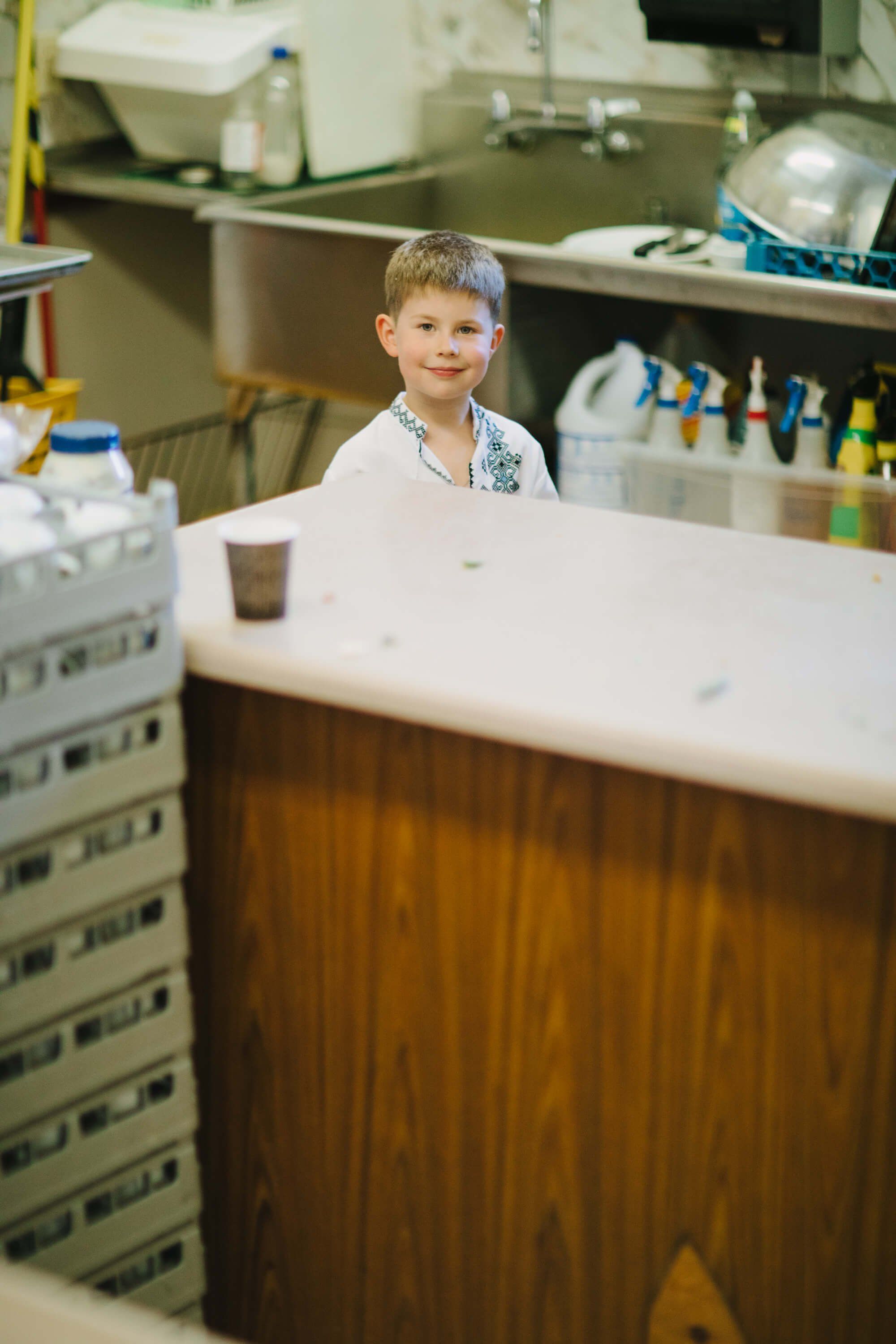 Young boy in white coat smiling at laboratory counter surrounded by scientific equipment and supplies