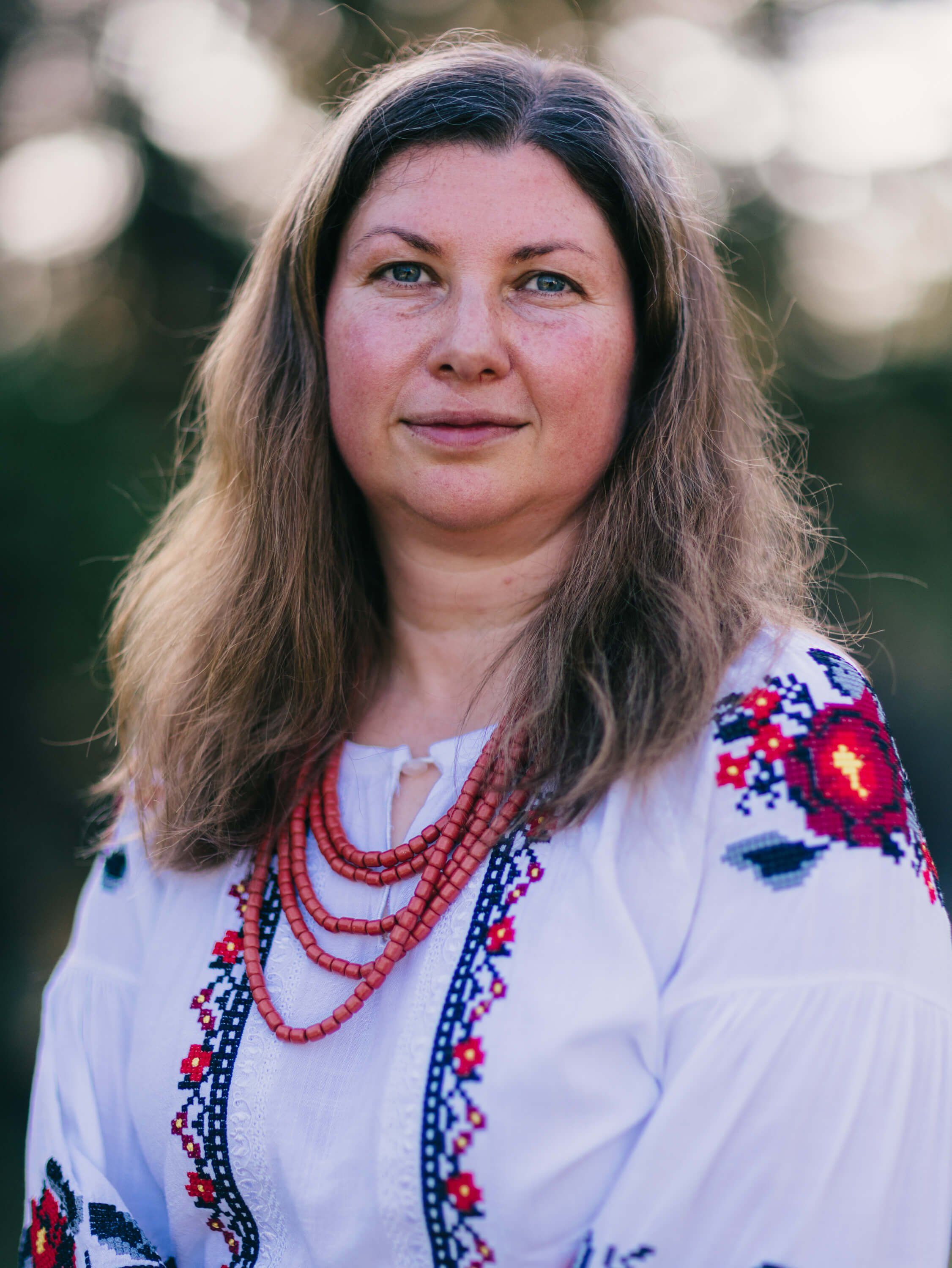 Woman in white embroidered Ukrainian blouse with red beaded necklaces, soft golden hour light, outdoor garden setting
