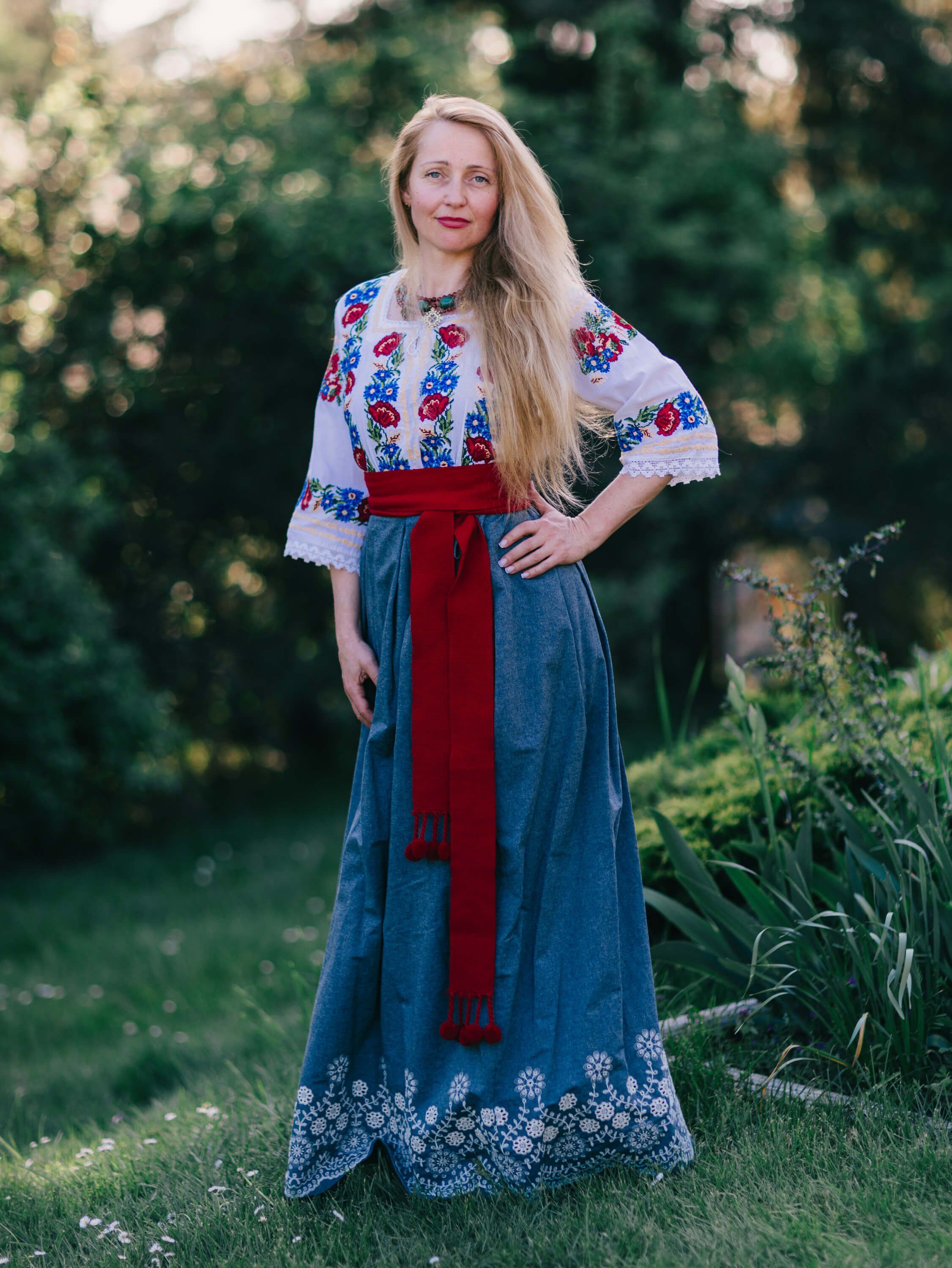 Woman in traditional Ukrainian embroidered dress with red sash standing in golden-hour garden light