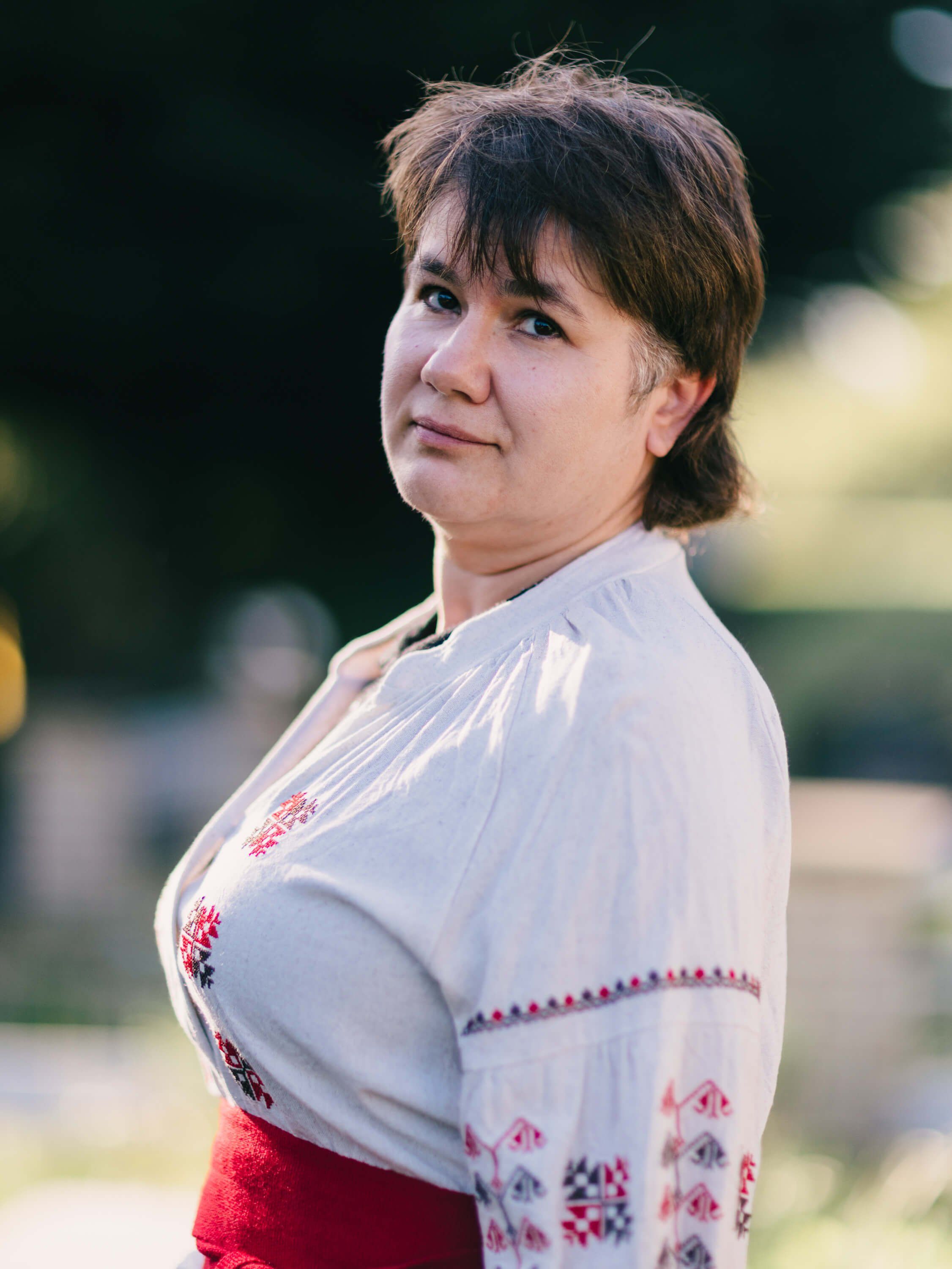Woman in embroidered white and red traditional Ukrainian dress smiles warmly at camera in soft outdoor light