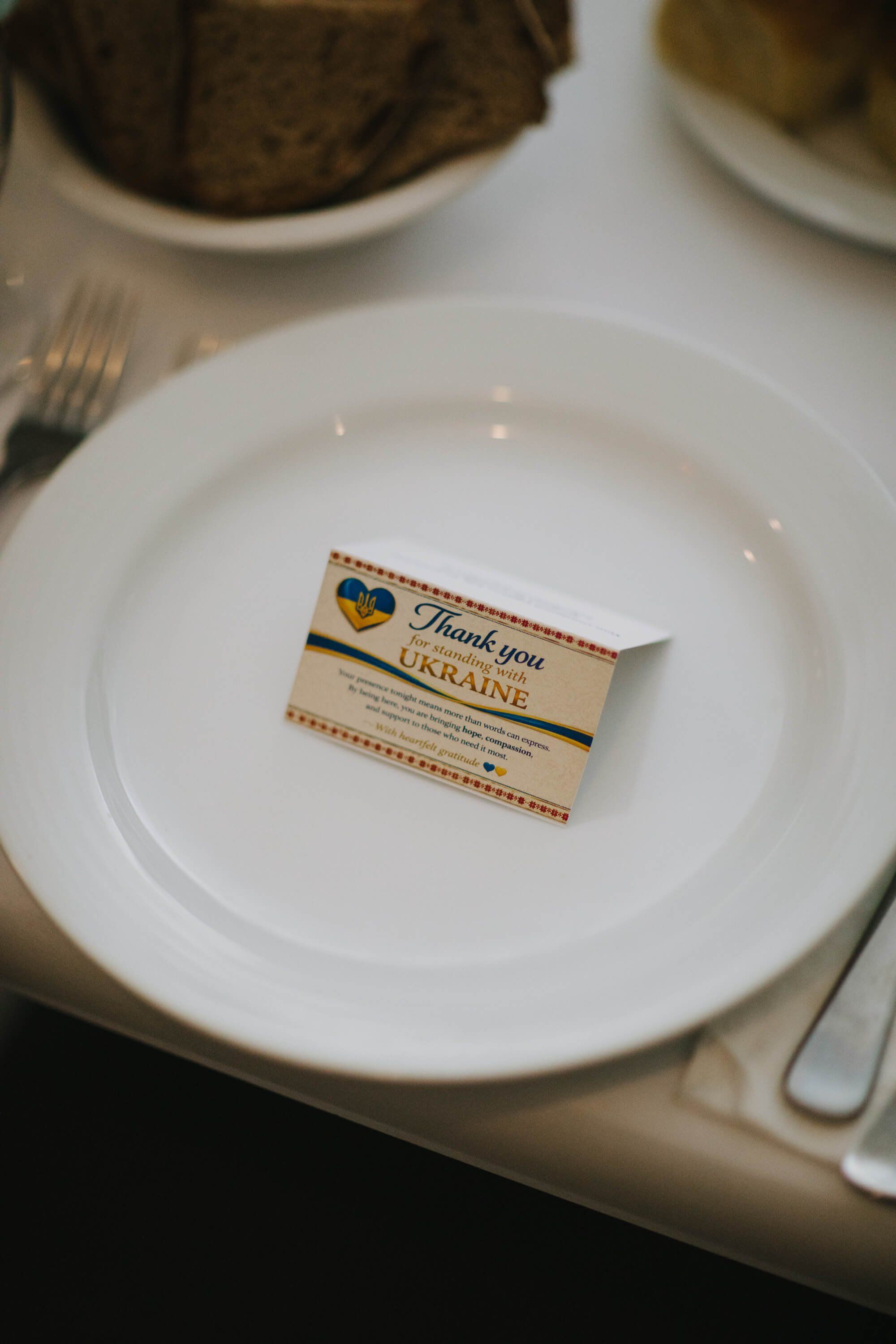 White plate with a small "Thank You Ukraine" ribbon favor tied with orange and blue striping, set at an elegant place setting