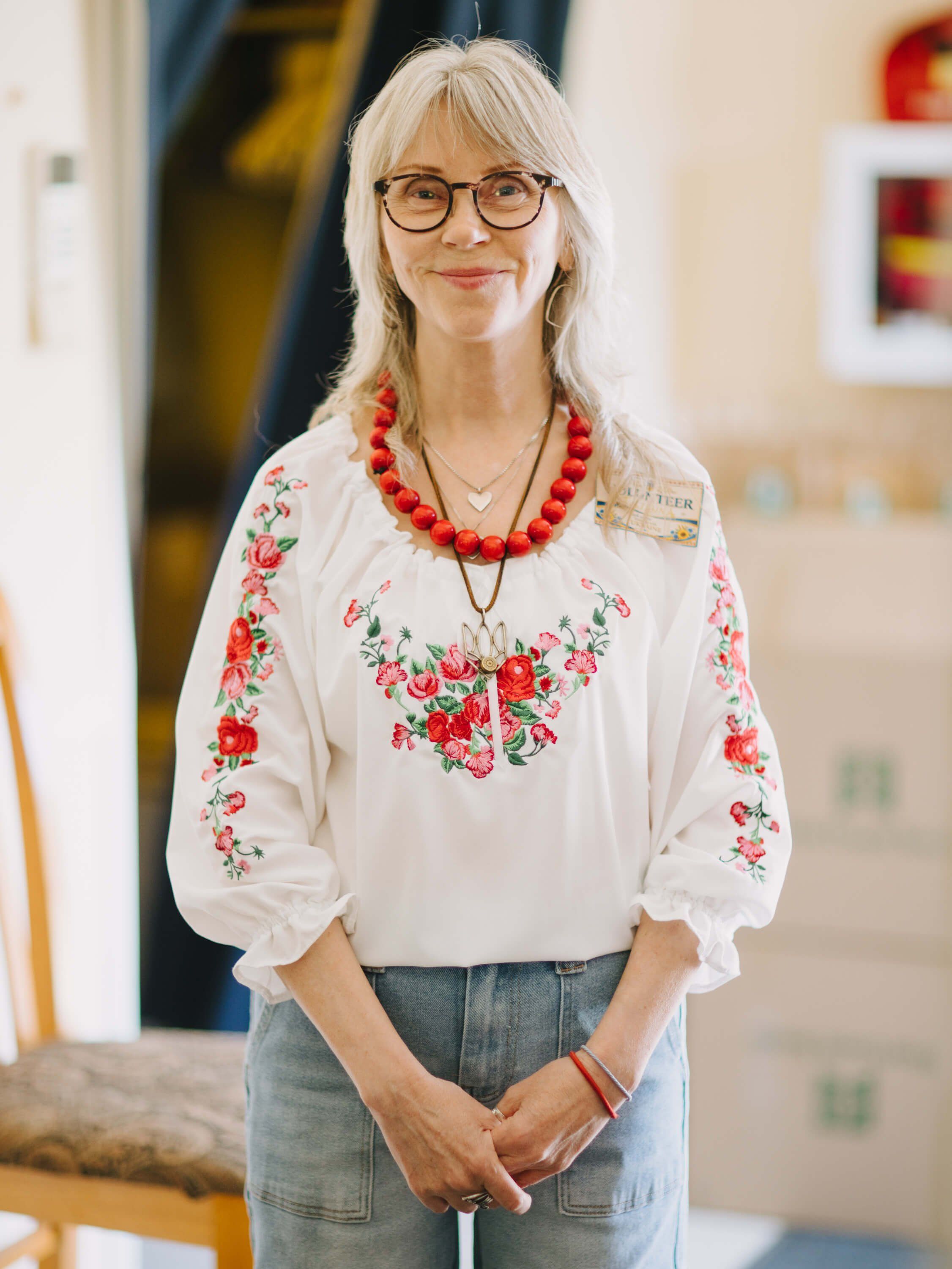 Woman in embroidered white blouse and red beaded necklace smiles at a Ukrainian fundraiser dinner event