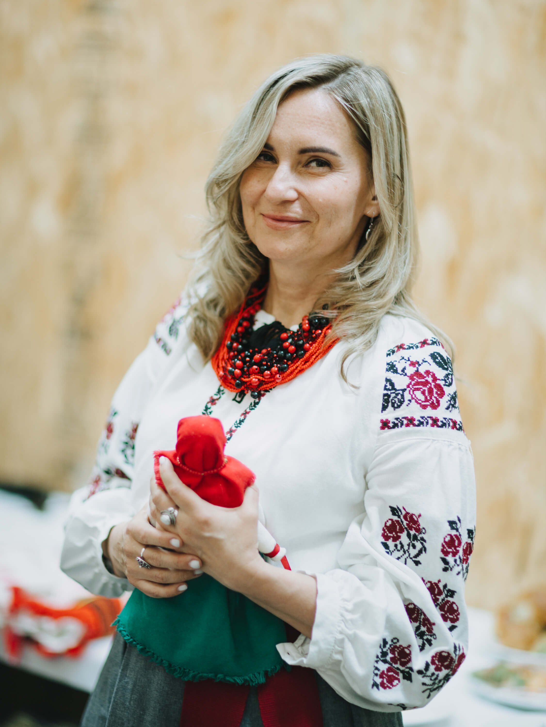 Woman in embroidered white blouse and red beaded necklace holds a red tulip at an indoor fundraiser event
