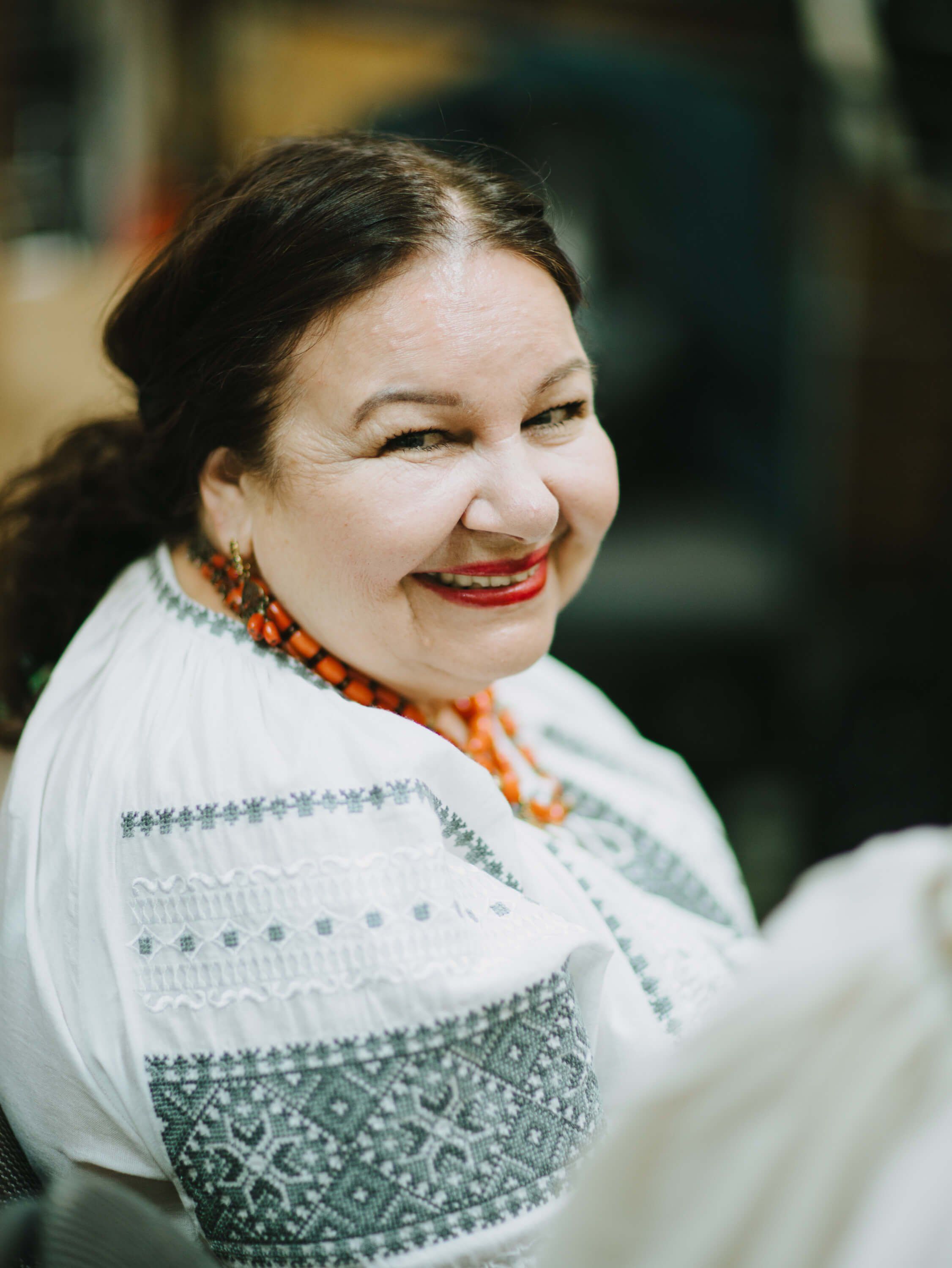 Woman in embroidered white shirt with orange beaded necklace smiles warmly over her shoulder at a Ukrainian fundraiser dinner