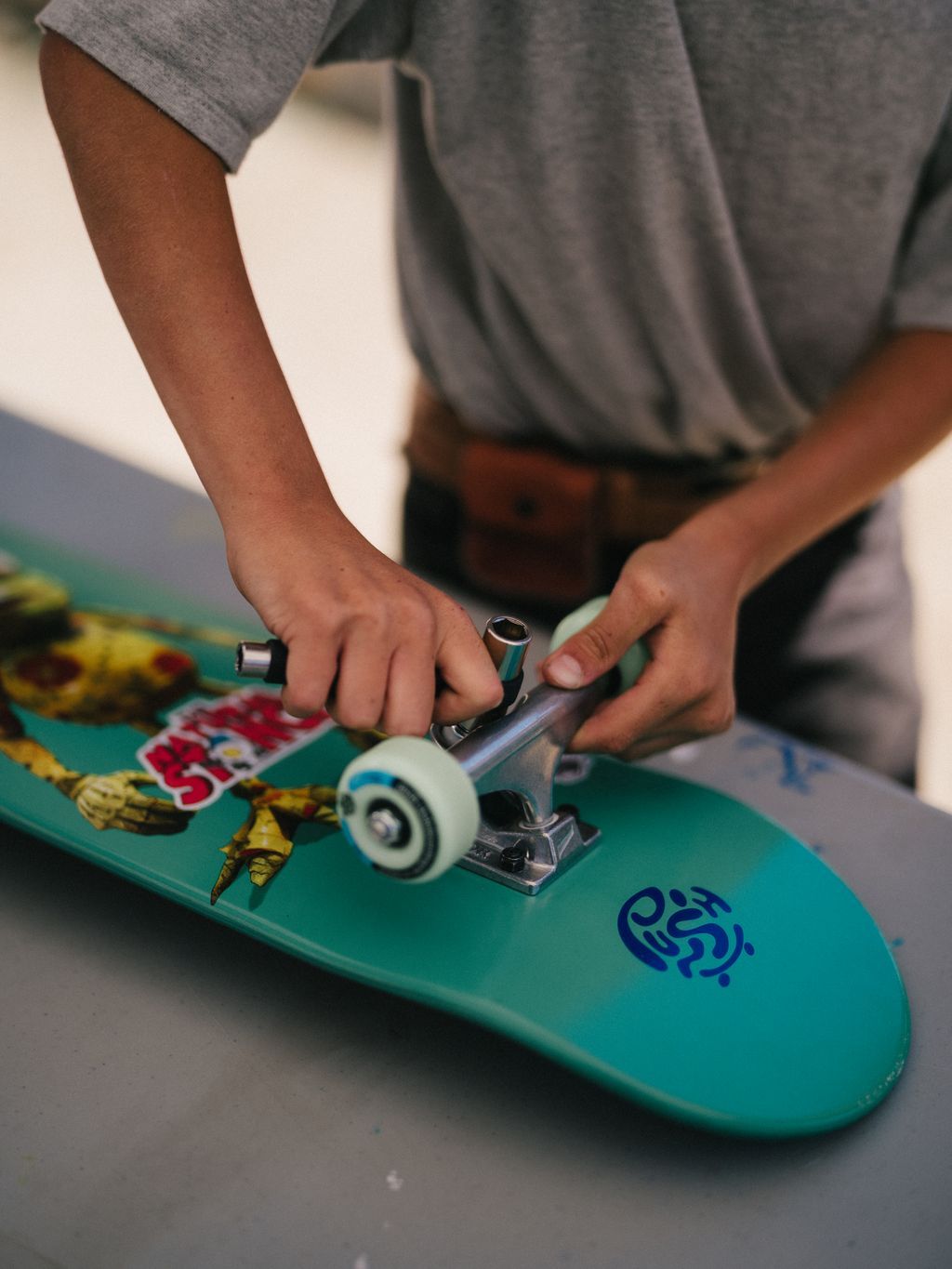 Hands adjusting a skateboard truck on a green deck at the Kanaka Road Skatepark during a community skate session
