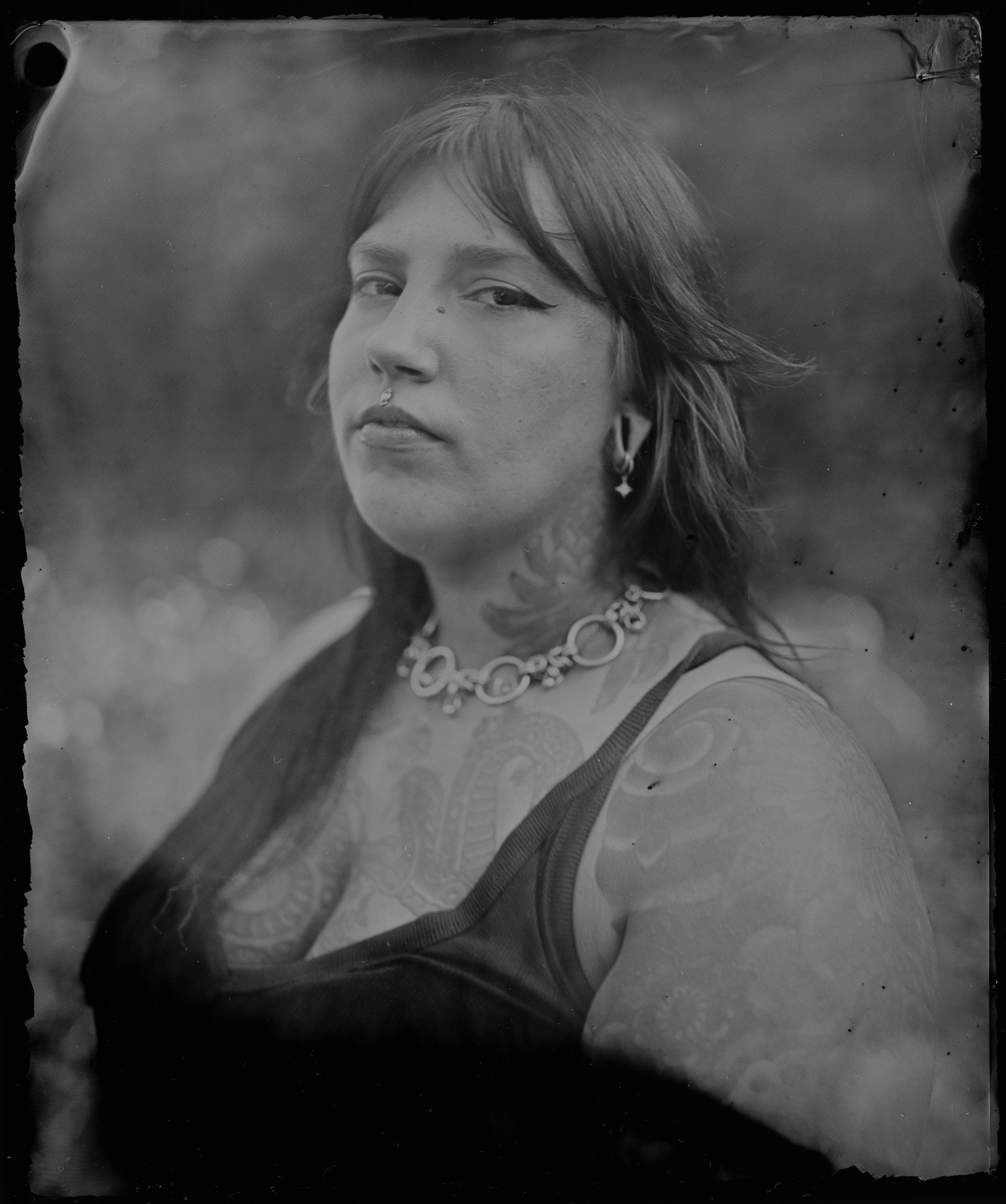 Woman in dark draped fabric and ornamental necklace gazes thoughtfully to the side in soft, diffused light