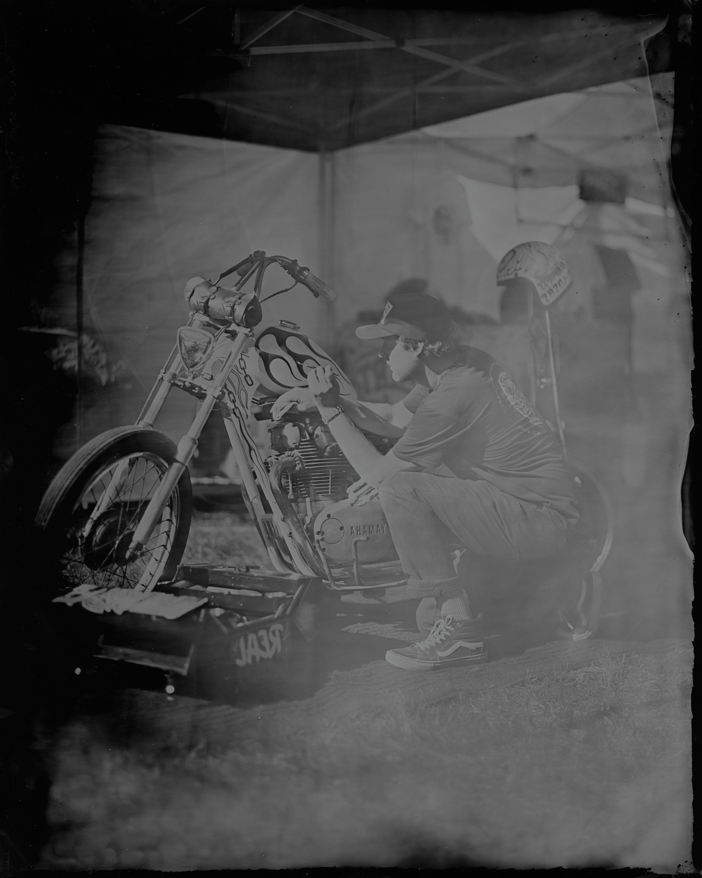 Skeletal figure adjusts vintage motorcycle in dramatic black and white studio lighting, casting haunting shadows on white backdrop