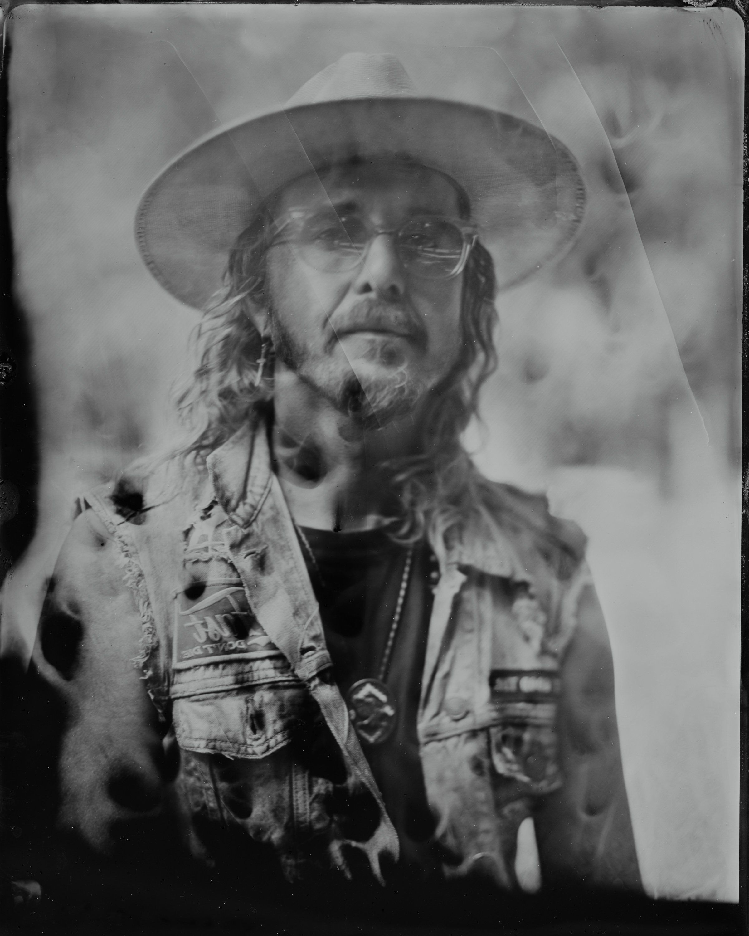 Bearded man in wide-brimmed hat and embroidered vest gazes thoughtfully, captured in moody black-and-white portrait photography