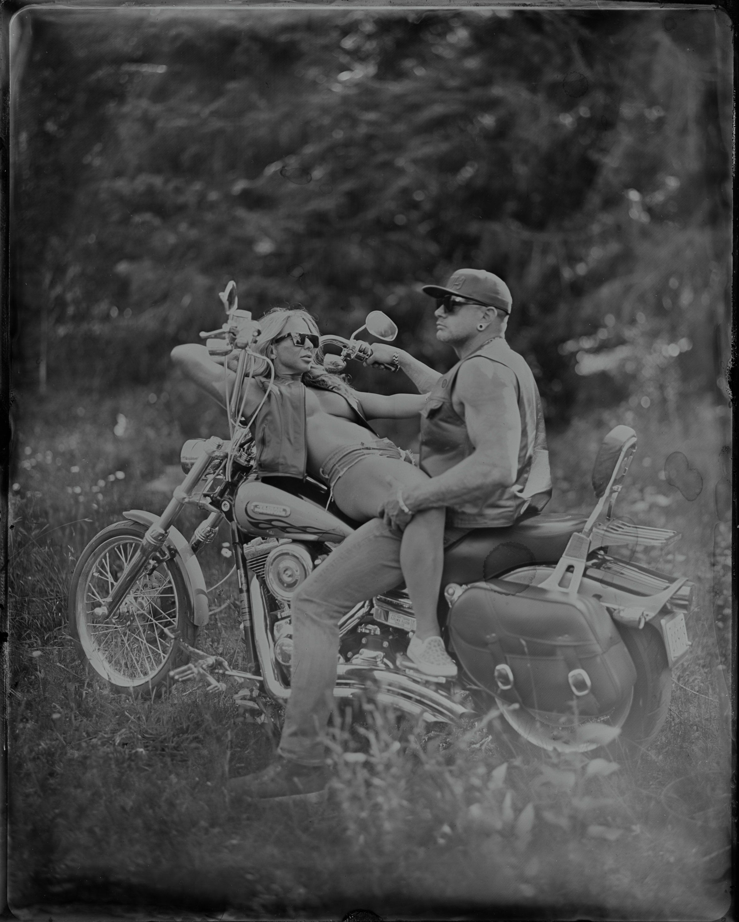 Two men on a vintage motorcycle with sidecar, laughing together in a black and white photograph with soft, natural outdoor light