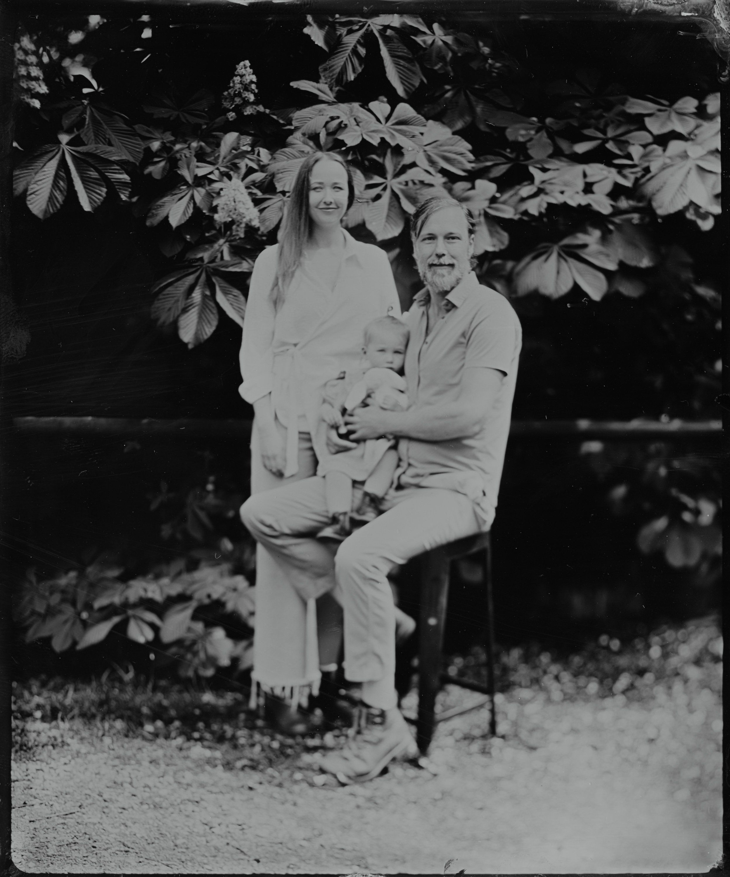 Couple with child seated beneath flowering branches in soft-focus garden setting, black and white vintage portrait