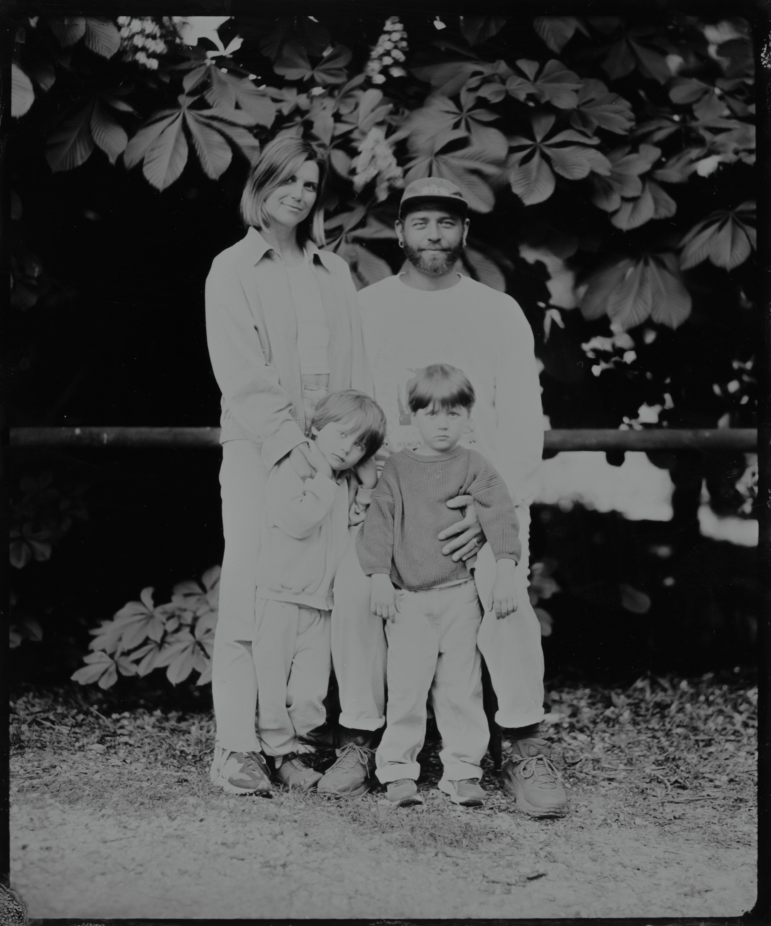 Three figures in light clothing stand beneath flowering branches in a black and white portrait, intimate and serene
