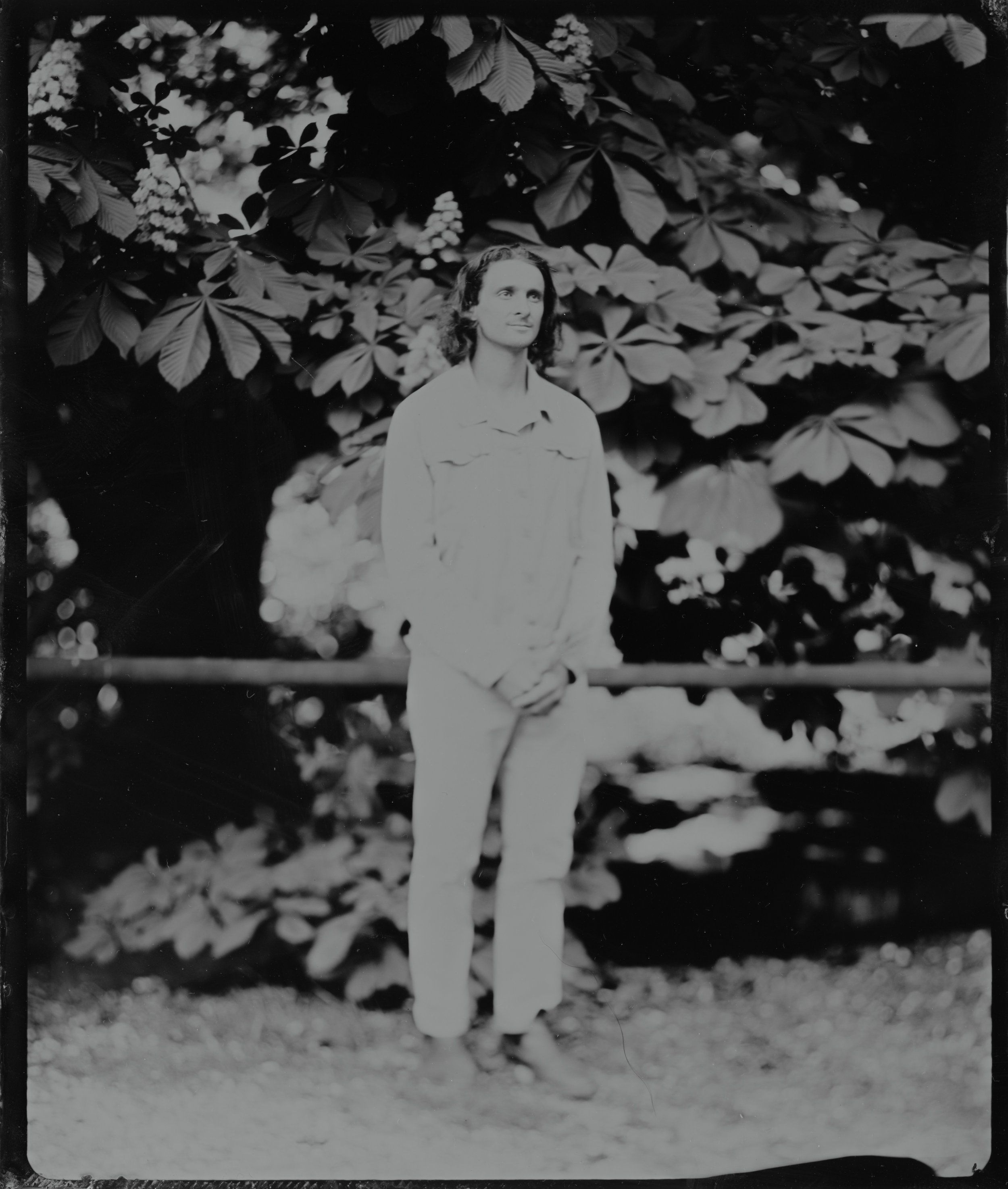 Black and white portrait of a woman in light clothing standing beneath flowering branches, looking upward in a contemplative moment