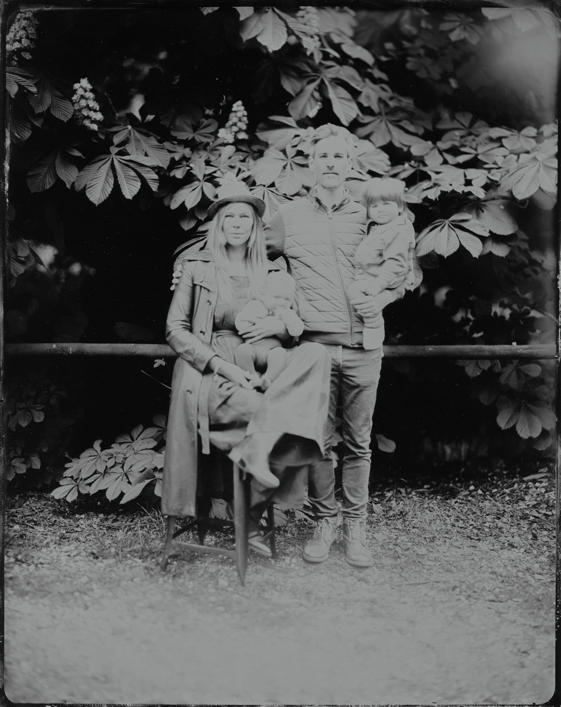 Couple seated together beneath leafy vines in dappled garden light, black and white vintage photograph