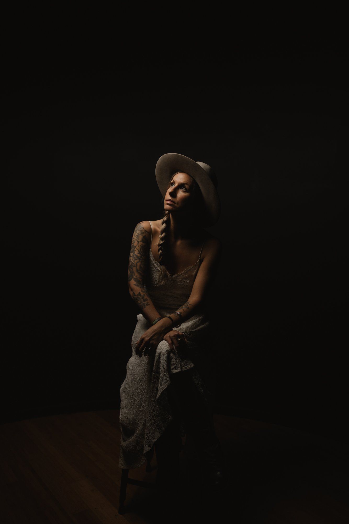 Woman in warm-toned sweater and hat gazes pensively against dark background, intimate studio lighting