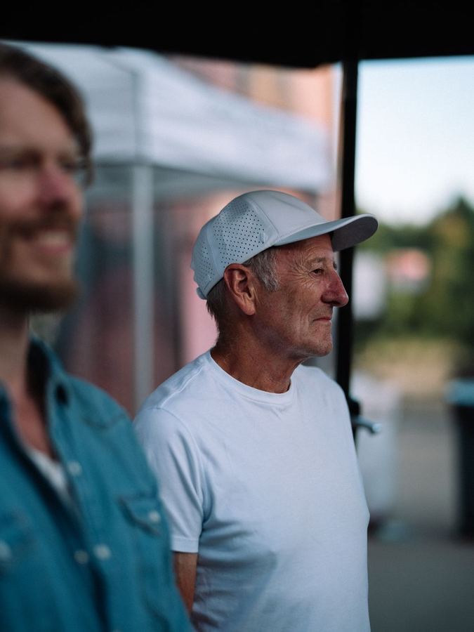 Man in white cap and t-shirt shown in profile against soft pink and blue evening light