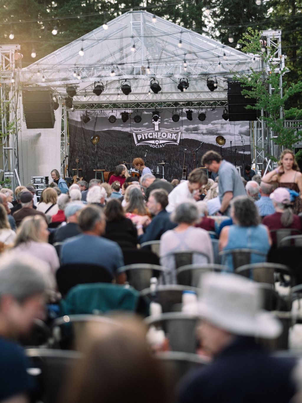 Crowd seated beneath clear-topped tent at Pitchfork Social with stage and lighting rig visible overhead