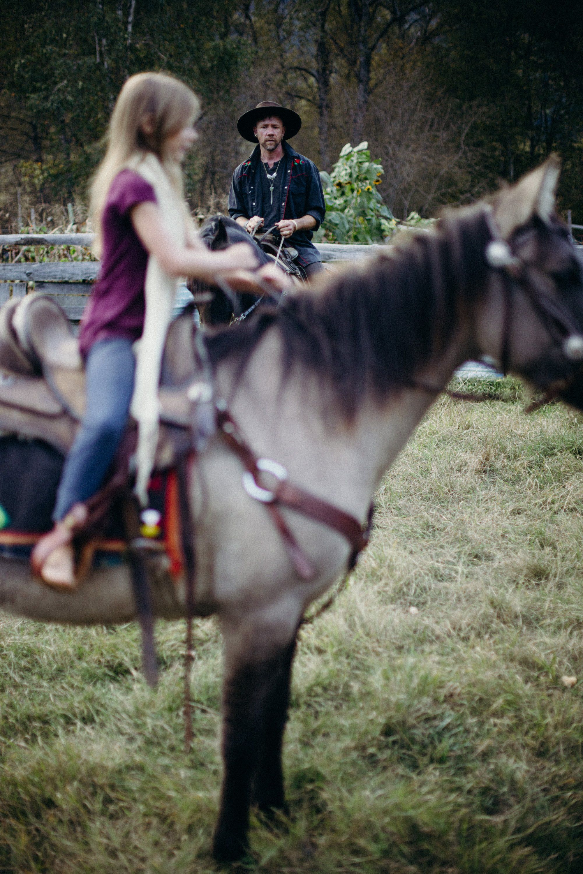 Child in purple top mounted on grey horse with instructor in black hat observing from grassy farm setting