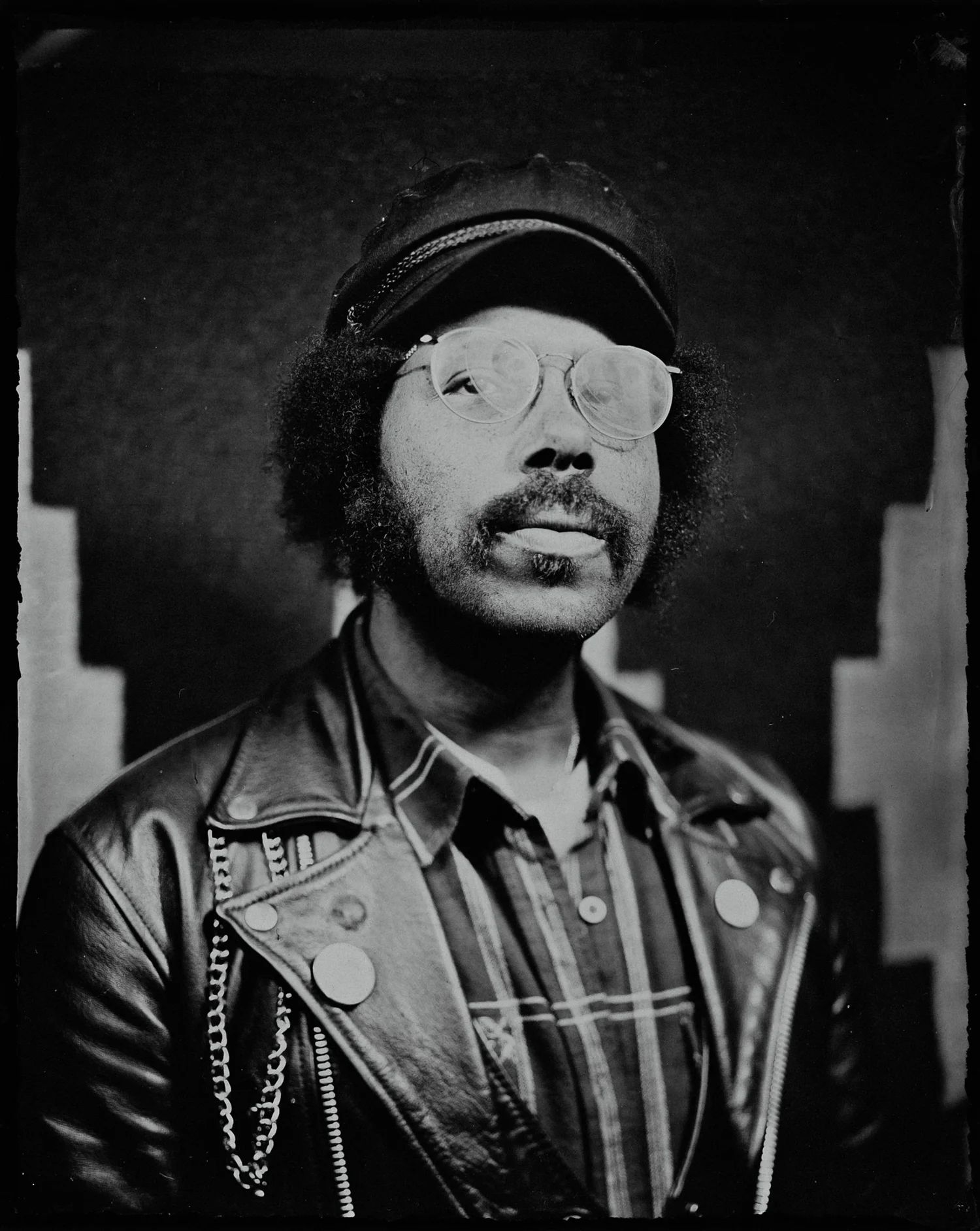 Man in glasses and winter hat gazes upward in contemplative black-and-white portrait, striped shirt visible against dark background