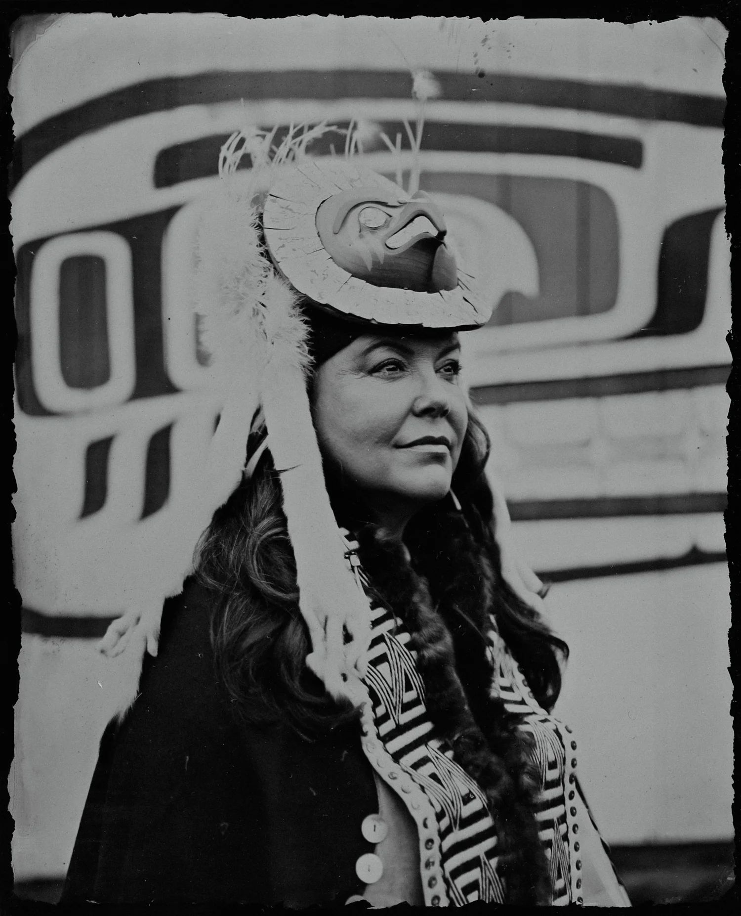 Woman wearing an elaborate feathered hat with curved design, striped shirt visible below, black and white archival photograph with soft focus background