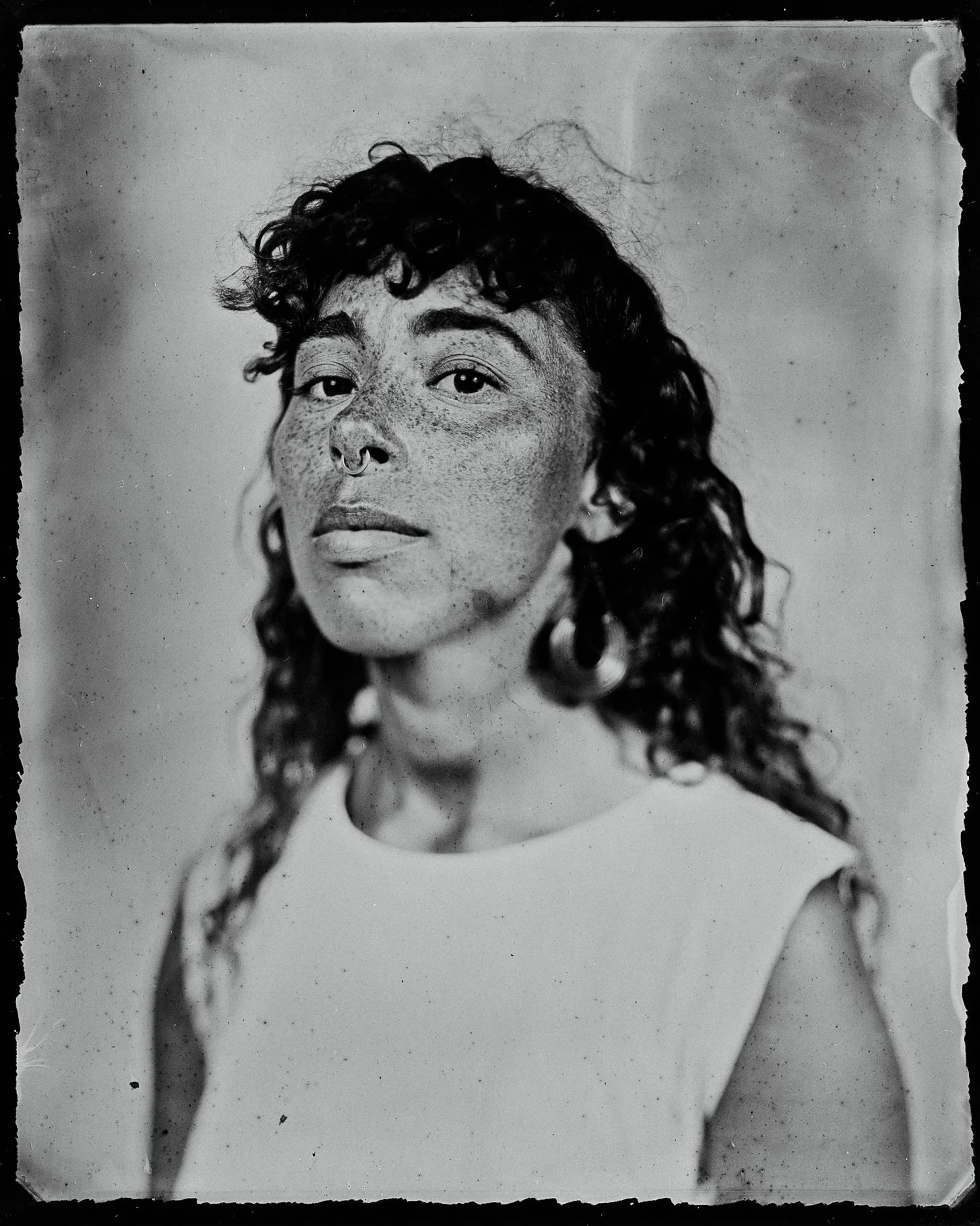 Black and white portrait of a person with dark wavy hair and freckles, gazing thoughtfully to the side in soft studio light