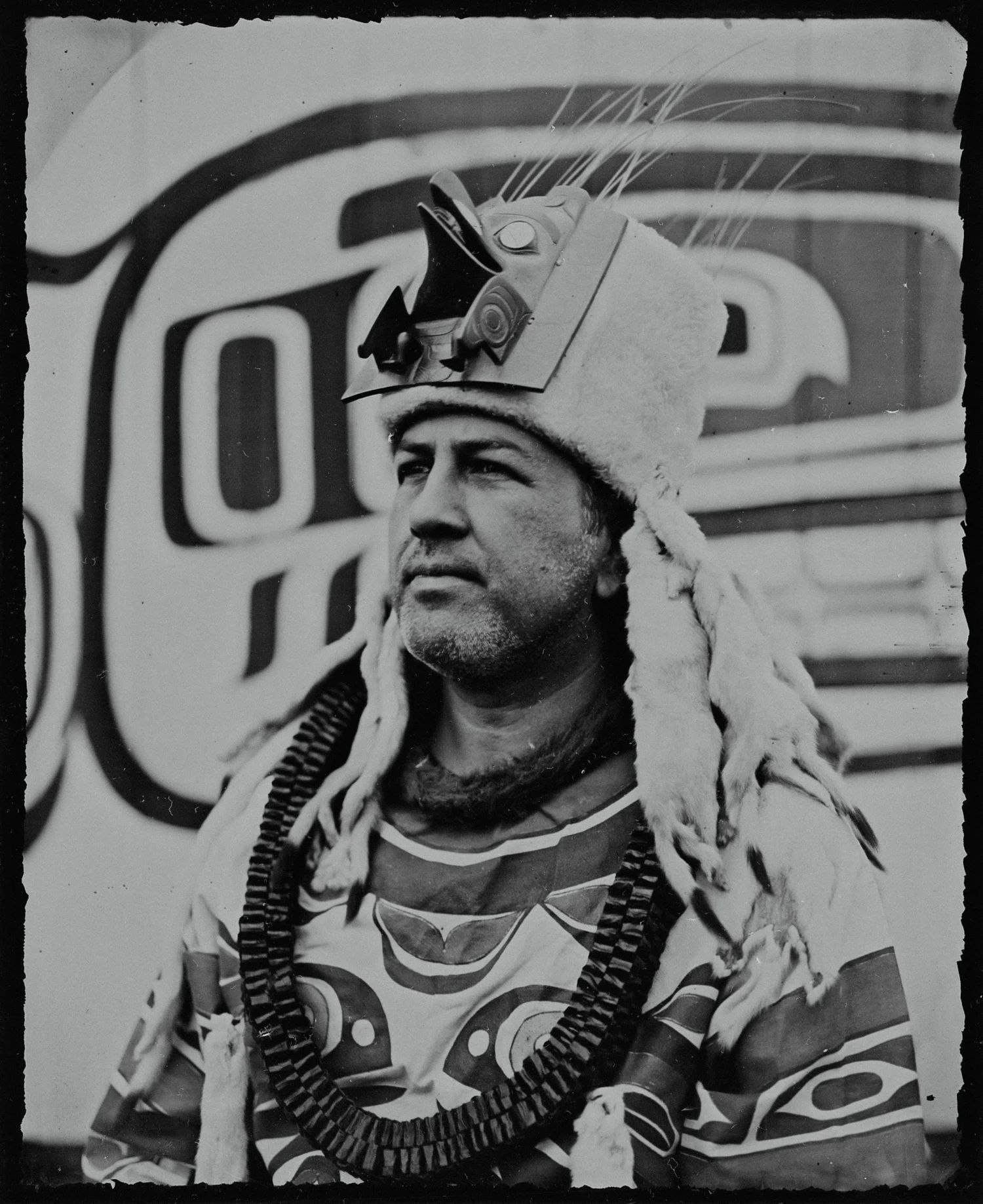 Man in ornate indigenous headdress and beaded regalia gazes thoughtfully to the side in this black and white portrait